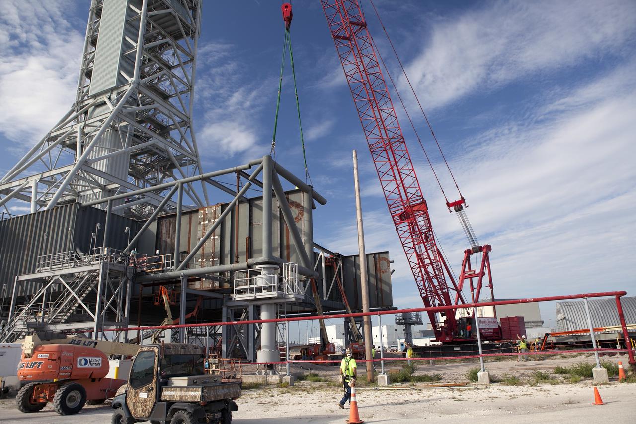 CAPE CANAVERAL, Fla. – Modifications continue on the Mobile Launcher, or ML, at the Mobile Launcher Park Site at NASA’s Kennedy Space Center in Florida. A crane is used to lift a section of the metal structure away from the ML. The ML is being modified and strengthened to accommodate the weight, size and thrust at launch of NASA's Space Launch System, or SLS, and Orion spacecraft.    In 2013, the agency awarded a contract to J.P. Donovan Construction Inc. of Rockledge, Fla., to modify the ML, which is one of the key elements of ground support equipment that is being upgraded by the Ground Systems Development and Operations Program office at Kennedy. The existing 24-foot exhaust hole is being enlarged and strengthened for the larger, heavier SLS rocket. The ML will carry the SLS rocket and Orion spacecraft to Launch Pad 39B for its first mission, Exploration Mission-1, in 2017. Photo credit: NASA/Daniel Casper