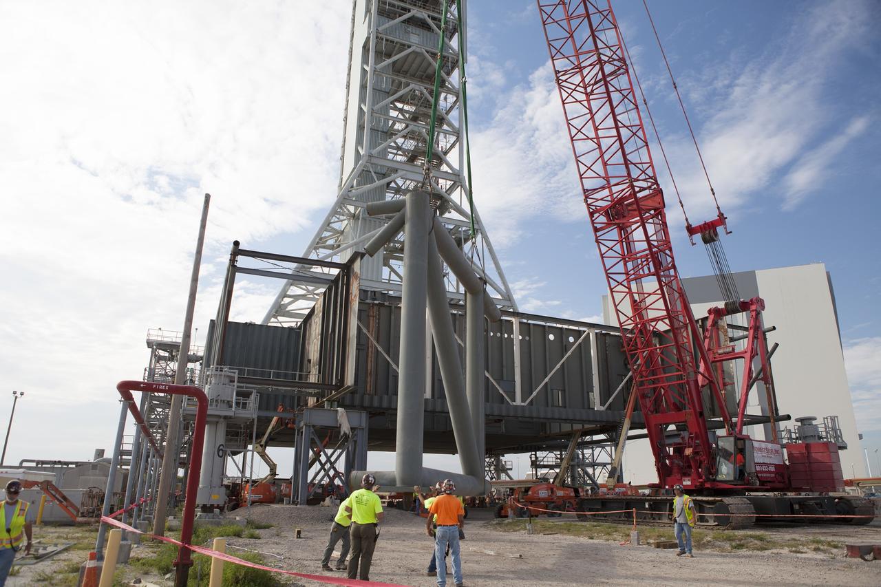 CAPE CANAVERAL, Fla. – Modifications continue on the Mobile Launcher, or ML, at the Mobile Launcher Park Site at NASA’s Kennedy Space Center in Florida. A section of the metal structure is lowered by crane to the ground near the ML. The ML is being modified and strengthened to accommodate the weight, size and thrust at launch of NASA's Space Launch System, or SLS, and Orion spacecraft.    In 2013, the agency awarded a contract to J.P. Donovan Construction Inc. of Rockledge, Fla., to modify the ML, which is one of the key elements of ground support equipment that is being upgraded by the Ground Systems Development and Operations Program office at Kennedy. The existing 24-foot exhaust hole is being enlarged and strengthened for the larger, heavier SLS rocket. The ML will carry the SLS rocket and Orion spacecraft to Launch Pad 39B for its first mission, Exploration Mission-1, in 2017. Photo credit: NASA/Daniel Casper