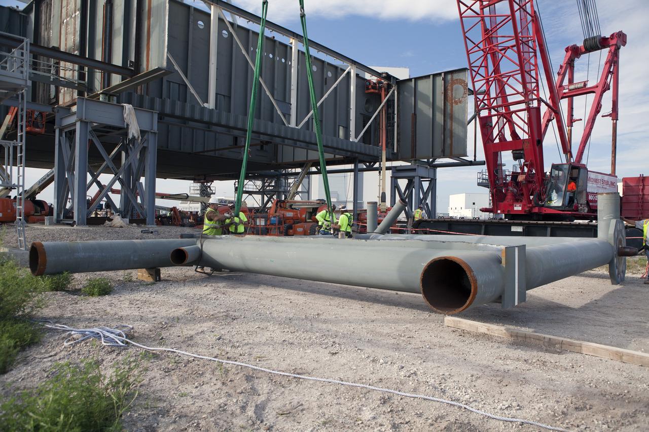 CAPE CANAVERAL, Fla. – Modifications continue on the Mobile Launcher, or ML, at the Mobile Launcher Park Site at NASA’s Kennedy Space Center in Florida. A section of the metal structure is lowered by crane to the ground near the ML. The ML is being modified and strengthened to accommodate the weight, size and thrust at launch of NASA's Space Launch System, or SLS, and Orion spacecraft.    In 2013, the agency awarded a contract to J.P. Donovan Construction Inc. of Rockledge, Fla., to modify the ML, which is one of the key elements of ground support equipment that is being upgraded by the Ground Systems Development and Operations Program office at Kennedy. The existing 24-foot exhaust hole is being enlarged and strengthened for the larger, heavier SLS rocket. The ML will carry the SLS rocket and Orion spacecraft to Launch Pad 39B for its first mission, Exploration Mission-1, in 2017. Photo credit: NASA/Daniel Casper