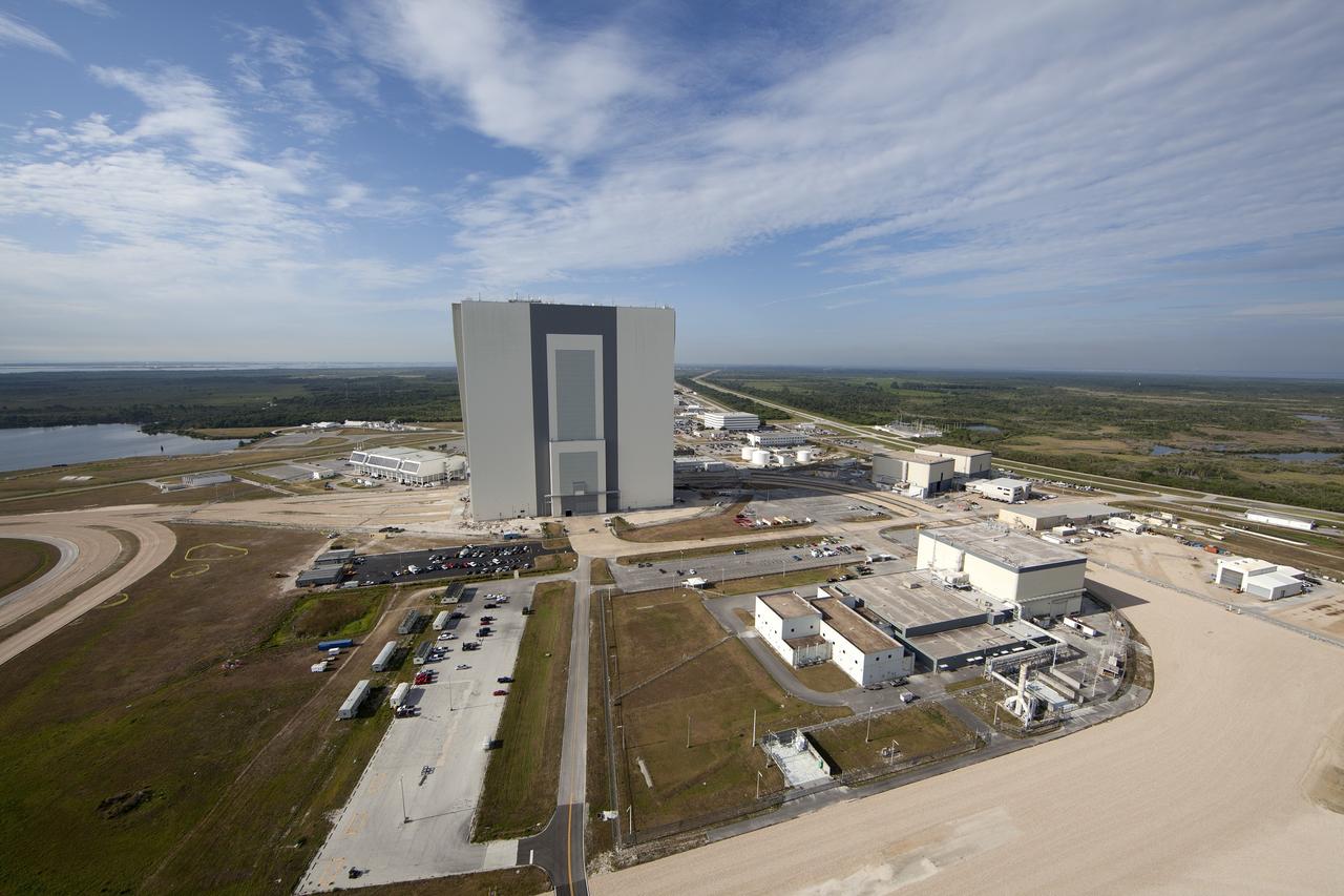 CAPE CANAVERAL, Fla. -- Modifications continue on the Mobile Launcher, or ML, at the Mobile Launcher Park Site at NASA’s Kennedy Space Center in Florida. In view from the top of the ML is the Vehicle Assembly Building, the Launch Control Center at left and various other facilities in the Launch Complex 39 area. The ML is being modified and strengthened to accommodate the weight, size and thrust at launch of NASA's Space Launch System, or SLS, and Orion spacecraft.    In 2013, the agency awarded a contract to J.P. Donovan Construction Inc. of Rockledge, Fla., to modify the ML, which is one of the key elements of ground support equipment that is being upgraded by the Ground Systems Development and Operations Program office at Kennedy. The existing 24-foot exhaust hole is being enlarged and strengthened for the larger, heavier SLS rocket. The ML will carry the SLS rocket and Orion spacecraft to Launch Pad 39B for its first mission, Exploration Mission-1, in 2017. Photo credit: NASA/Daniel Casper