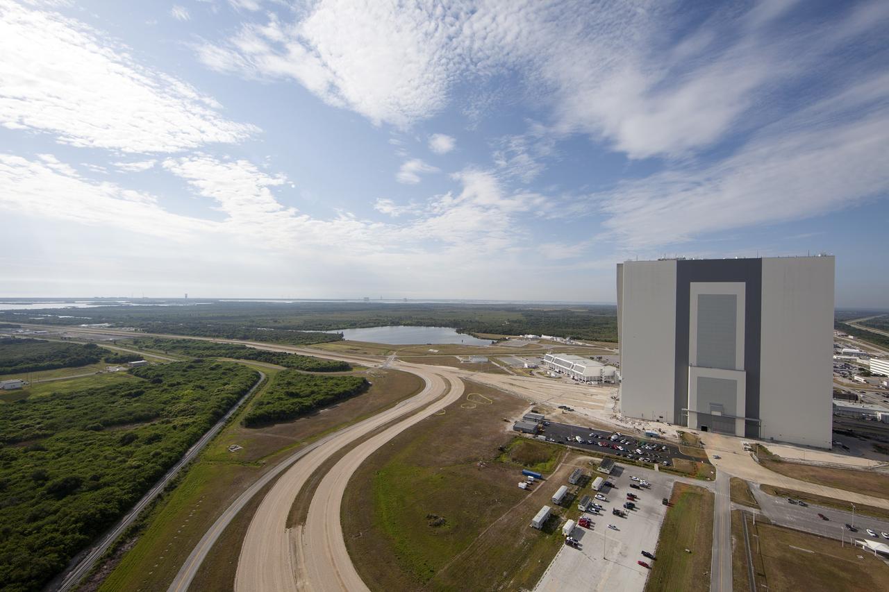CAPE CANAVERAL, Fla. -- Modifications continue on the Mobile Launcher, or ML, at the Mobile Launcher Park Site at NASA’s Kennedy Space Center in Florida. In view from the top of the ML is the Vehicle Assembly Building, the Launch Control Center at left and various other facilities in the Launch Complex 39 area. The ML is being modified and strengthened to accommodate the weight, size and thrust at launch of NASA's Space Launch System, or SLS, and Orion spacecraft.    In 2013, the agency awarded a contract to J.P. Donovan Construction Inc. of Rockledge, Fla., to modify the ML, which is one of the key elements of ground support equipment that is being upgraded by the Ground Systems Development and Operations Program office at Kennedy. The existing 24-foot exhaust hole is being enlarged and strengthened for the larger, heavier SLS rocket. The ML will carry the SLS rocket and Orion spacecraft to Launch Pad 39B for its first mission, Exploration Mission-1, in 2017. Photo credit: NASA/Daniel Casper