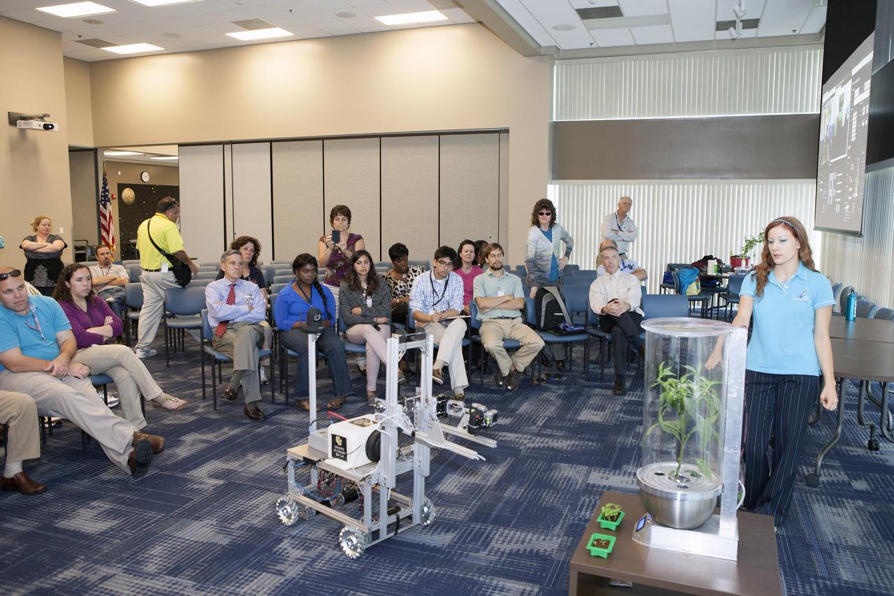 CAPE CANAVERAL, Fla. -- At the Kennedy Space Center in Florida, Heather Hava, right, who is working on a doctorate in aerospace engineering sciences at the University of Colorado Boulder, describes a computerized SmartPot, or SPOT, which could be used to grow plants in a deep-space habitat. The SPOTs could be tended by a Remotely Operated Gardening Rover, or ROGR, seen on the left. The system is being developed by the graduate students participating in the eXploration HABitat X-Hab Academic Innovation Challenge.      X-Hab Academic Innovation Challenge is a university-level activity designed to engage and retain students in science, technology, engineering and math, or STEM, disciplines. NASA will directly benefit from the effort by sponsoring the development of innovative habitat concepts from universities which may result in innovative ideas and solutions that could be applied to exploration habitats. For more: http://www.nasa.gov/exploration/technology/deep_space_habitat/xhab/ Photo credit: NASA/Daniel Casper