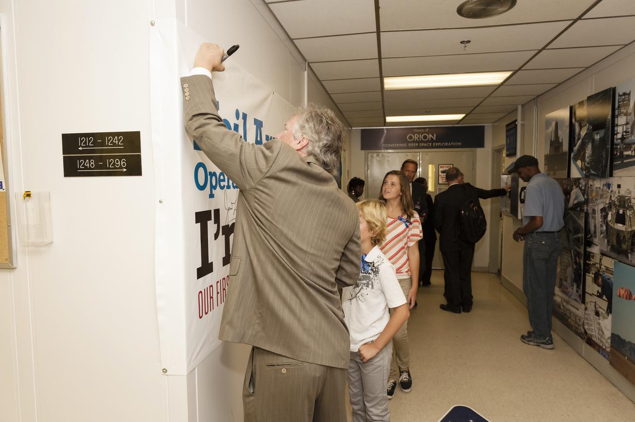 CAPE CANAVERAL, Fla. -- Family members of Apollo 11 astronaut Neil Armstrong sign a banner displaying the new name of the Operations and Checkout Building at NASA's Kennedy Space Center in Florida. The banner signing followed a ceremony renaming the refurbished building for Apollo 11 astronaut Neil Armstrong, the first person to set foot on the moon. From left are Armstrong's son Rick, his grandson Bryce and his granddaughter Lily. The building's high bay is being used to support the agency's new Orion spacecraft and is the same spaceport facility where the Apollo 11 command/service module and lunar module were prepped for the first lunar landing mission in 1969. Orion is designed to take humans farther than they’ve ever gone before, serving as the exploration vehicle that will carry astronauts to deep space and sustain the crew during travel to destinations such as an asteroid or Mars.    The ceremony was part of NASA's 45th anniversary celebration of the Apollo 11 moon landing. As the world watched, Neil Armstrong and Buzz Aldrin landed in the moon's Sea of Tranquility on July 20, 1969, aboard the lunar module Eagle. Meanwhile, crewmate Michael Collins orbited above in the command module Columbia. For more, visit http://www.nasa.gov/press/2014/july/nasa-honors-historic-first-moon-landing-eyes-first-mars-mission. Photo credit: NASA/Kevin O'Connell