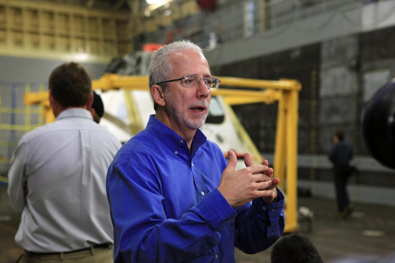LOS ANGELES, Calif. – Mark Geyer, NASA Orion Program manager, talks with reporters in the well deck of the USS Anchorage after completion of Underway Recovery Test 2. NASA, Lockheed Martin and the U.S. Navy completed the recovery test on the Orion boilerplate test vehicle in the Pacific Ocean off the coast of San Diego to prepare for recovery of the Orion crew module on its return from a deep space mission. The underway recovery test allowed the teams to demonstrate and evaluate the recovery processes, procedures, new hardware and personnel in open waters. Behind Geyer is the test vehicle secured in its recovery cradle. The U.S. Navy ship is in Los Angeles for LA Navy Days. The Ground Systems Development and Operations Program conducted the underway recovery test. Orion is the exploration spacecraft designed to carry astronauts to destinations not yet explored by humans, including an asteroid and Mars. It will have emergency abort capability, sustain the crew during space travel and provide safe re-entry from deep space return velocities. The first unpiloted test flight of the Orion is scheduled to launch in 2014 atop a Delta IV rocket and in 2017 on NASA’s Space Launch System rocket. For more information, visit http://www.nasa.gov/orion. Photo credit: Kim Shiflett