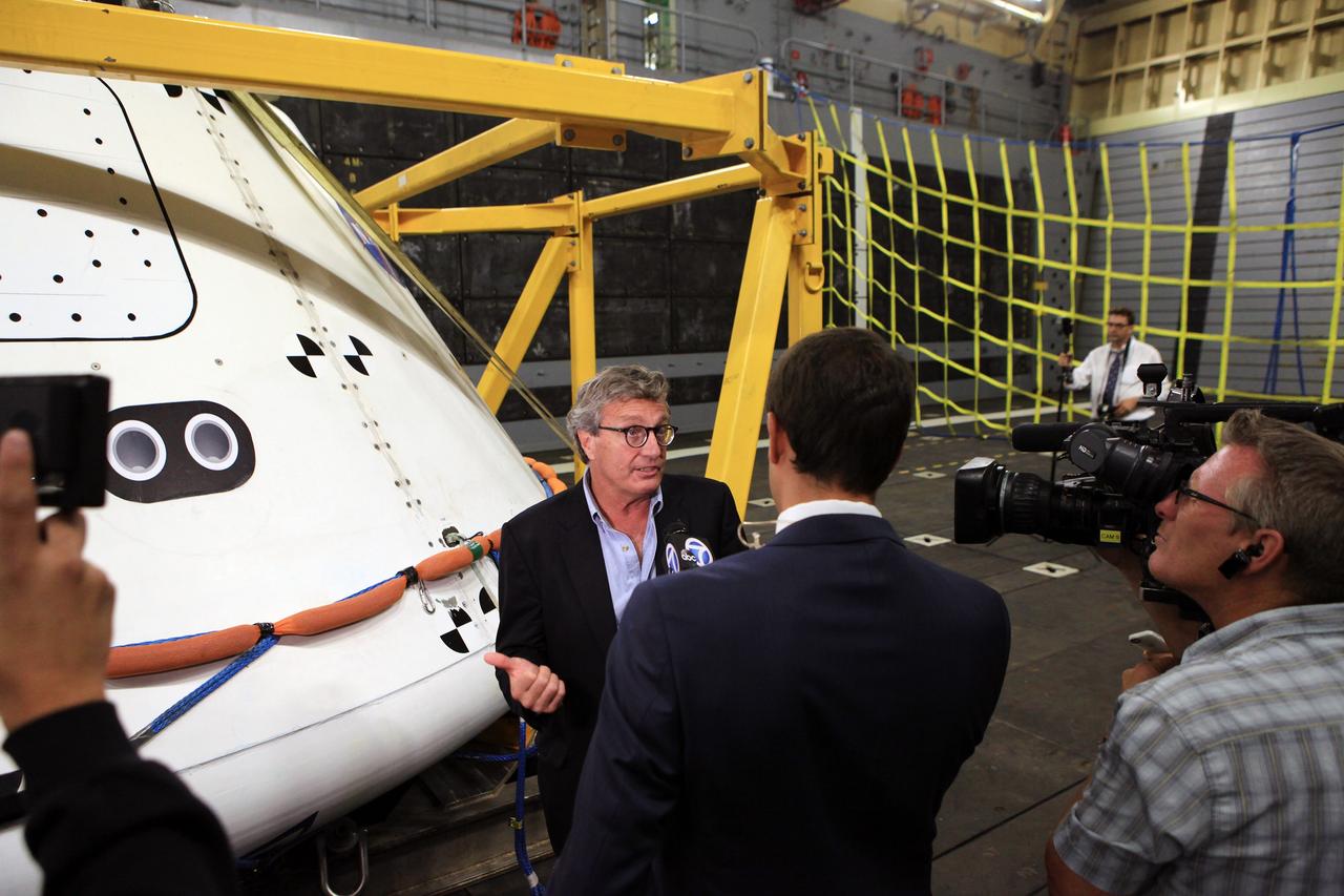 LOS ANGELES, Calif. – Larry Price, Lockheed Martin Space Systems deputy program manager for Orion, talks with reporters in the well deck of the USS Anchorage after completion of Underway Recovery Test 2. Behind him is the Orion boilerplate test vehicle secured in its recovery cradle. NASA, Lockheed Martin and the U.S. Navy completed the recovery test in the Pacific Ocean off the coast of San Diego to prepare for recovery of the Orion crew module on its return from a deep space mission. The underway recovery test allowed the teams to demonstrate and evaluate the recovery processes, procedures, new hardware and personnel in open waters. The U.S. Navy ship is in Los Angeles for LA Navy Days. The Ground Systems Development and Operations Program conducted the underway recovery test. Orion is the exploration spacecraft designed to carry astronauts to destinations not yet explored by humans, including an asteroid and Mars. It will have emergency abort capability, sustain the crew during space travel and provide safe re-entry from deep space return velocities. The first unpiloted test flight of the Orion is scheduled to launch in 2014 atop a Delta IV rocket and in 2017 on NASA’s Space Launch System rocket. For more information, visit http://www.nasa.gov/orion. Photo credit: Kim Shiflett