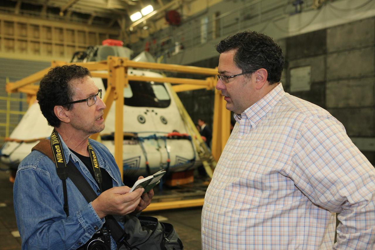 LOS ANGELES, Calif. – Todd May, NASA Space Launch System Program manager, talks with a reporter in the well deck of the USS Anchorage after completion of Underway Recovery Test 2. Behind him is the Orion boilerplate test vehicle secured in its recovery cradle. NASA, Lockheed Martin and the U.S. Navy completed the recovery test in the Pacific Ocean off the coast of San Diego to prepare for recovery of the Orion crew module on its return from a deep space mission. The underway recovery test allowed the teams to demonstrate and evaluate the recovery processes, procedures, new hardware and personnel in open waters. The U.S. Navy ship is in Los Angeles for LA Navy Days. The Ground Systems Development and Operations Program conducted the underway recovery test. Orion is the exploration spacecraft designed to carry astronauts to destinations not yet explored by humans, including an asteroid and Mars. It will have emergency abort capability, sustain the crew during space travel and provide safe re-entry from deep space return velocities. The first unpiloted test flight of the Orion is scheduled to launch in 2014 atop a Delta IV rocket and in 2017 on NASA’s Space Launch System rocket. For more information, visit http://www.nasa.gov/orion. Photo credit: Kim Shiflett