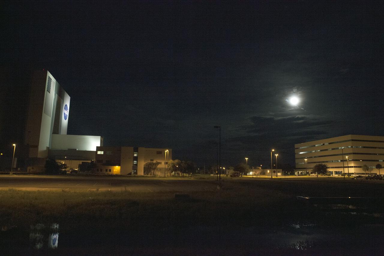 CAPE CANAVERAL, Fla. – A “supermoon” is partially obscured by the clouds over Launch Complex 39 at NASA’s Kennedy Space Center in Florida. At left, the 525-foot-tall Vehicle Assembly Building, illuminated by artificial light, threatens to outshine the moon.    The scientific term for the supermoon phenomenon is "perigee moon." Full moons vary in size because of the oval shape of the moon's orbit. The moon follows an elliptical path around Earth with one side about 50,000 kilometers closer than the other. Full moons that occur on the perigee side of the moon's orbit seem extra big and bright. For additional information, visit http://science.nasa.gov/science-news/science-at-nasa/2014/10jul_supermoons/. Photo credit: NASA/Ben Smegelsky