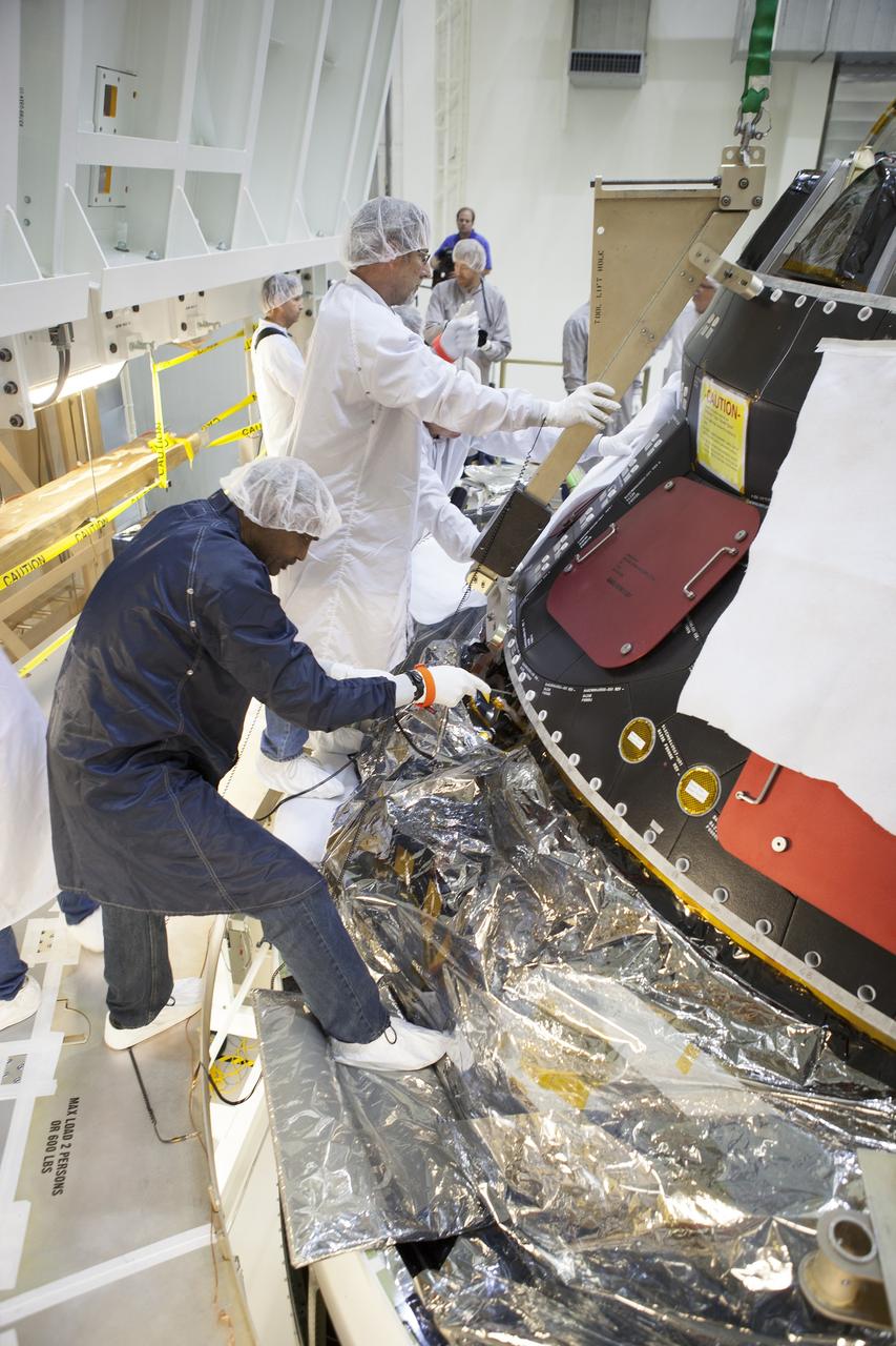CAPE CANAVERAL, Fla. – Inside the Operations and Checkout Building high bay at NASA's Kennedy Space Center in Florida, technicians dressed in clean-room suits attach the middle back shell tile panel onto the Orion crew module. Preparations are underway for Exploration Flight Test-1, or EFT-1. Orion is the exploration spacecraft designed to carry astronauts to destinations not yet explored by humans, including an asteroid and Mars. It will have emergency abort capability, sustain the crew during space travel and provide safe re-entry from deep space return velocities. The first unpiloted test flight of the Orion is scheduled to launch later this year atop a Delta IV rocket from Cape Canaveral Air Force Station in Florida to an altitude of 3,600 miles above the Earth's surface. The two-orbit, four-hour flight test will help engineers evaluate the systems critical to crew safety including the heat shield, parachute system and launch abort system. For more information, visit http://www.nasa.gov/orion. Photo credit: NASA/Dimitri Gerondidakis