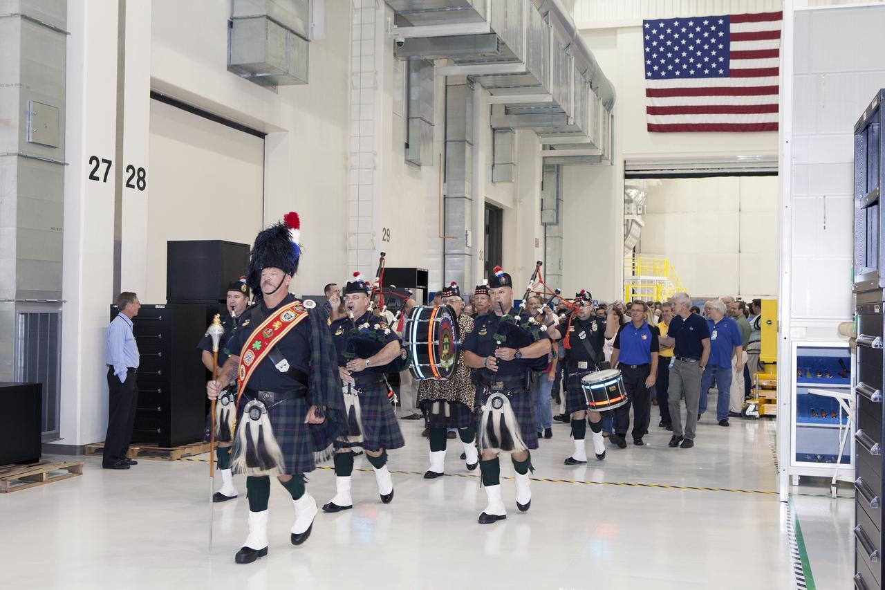 CAPE CANAVERAL, Fla. – Inside the Neil Armstrong Operations and Checkout Building high bay at NASA's Kennedy Space Center in Florida, members of the Brevard Police and Fire Pipes and Drums lead NASA and Lockheed Martin workers toward the Orion crew module, stacked atop its service module. A ceremony will begin to officially turn over the Orion spacecraft for Exploration Flight Test-1 to Lockheed Martin Ground Operations from Orion Assembly, Integration and Production.    Orion is the exploration spacecraft designed to carry astronauts to destinations not yet explored by humans, including an asteroid and Mars. It will have emergency abort capability, sustain the crew during space travel and provide safe re-entry from deep space return velocities. The first unpiloted test flight of the Orion is scheduled to launch atop a United Launch Alliance Delta IV Heavy rocket from Cape Canaveral Air Force Station in Florida in December to an altitude of 3,600 miles above the Earth's surface. The two-orbit, four-hour flight test will help engineers evaluate the systems critical to crew safety including the heat shield, parachute system and launch abort system. For more information, visit http://www.nasa.gov/orion. Photo credit: NASA/Daniel Casper