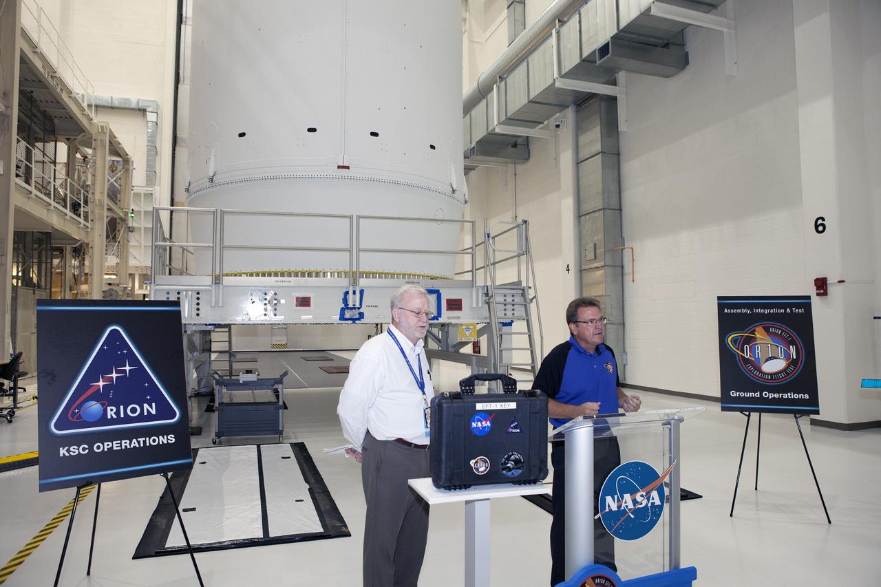 CAPE CANAVERAL, Fla. – Inside the Neil Armstrong Operations and Checkout Building high bay at NASA's Kennedy Space Center in Florida, Jules Schneider, at right, Lockheed Martin Orion Production Operations manager, speaks to NASA and Lockheed Martin workers during a ceremony to turn over the Orion spacecraft for Exploration Flight Test-1 to Ground Operations. At left is Blake Hale, Lockheed Martin Ground Operations manager. Orion is the exploration spacecraft designed to carry astronauts to destinations not yet explored by humans, including an asteroid and Mars. It will have emergency abort capability, sustain the crew during space travel and provide safe re-entry from deep space return velocities. The first unpiloted test flight of the Orion is scheduled to launch atop a United Launch Alliance Delta IV Heavy rocket from Cape Canaveral Air Force Station in Florida in December to an altitude of 3,600 miles above the Earth's surface. The two-orbit, four-hour flight test will help engineers evaluate the systems critical to crew safety including the heat shield, parachute system and launch abort system. For more information, visit http://www.nasa.gov/orion. Photo credit: NASA/Daniel Casper