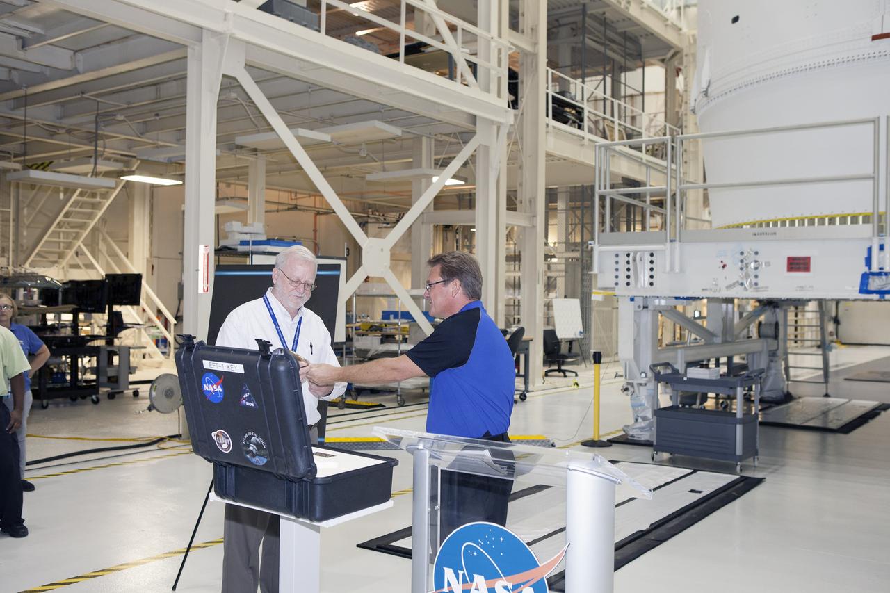 CAPE CANAVERAL, Fla. – During a ceremony inside the Neil Armstrong Operations and Checkout Building high bay at NASA's Kennedy Space Center in Florida, Jules Schneider, at right, Lockheed Martin Orion Production Operations manager, presents the key to symbolically turn over the Orion spacecraft for Exploration Flight Test-1 to Ground Operations. Accepting the key is Blake Hale, Lockheed Martin Ground Operations manager. Orion is the exploration spacecraft designed to carry astronauts to destinations not yet explored by humans, including an asteroid and Mars. It will have emergency abort capability, sustain the crew during space travel and provide safe re-entry from deep space return velocities. The first unpiloted test flight of the Orion is scheduled to launch atop a United Launch Alliance Delta IV Heavy rocket from Cape Canaveral Air Force Station in Florida in December to an altitude of 3,600 miles above the Earth's surface. The two-orbit, four-hour flight test will help engineers evaluate the systems critical to crew safety including the heat shield, parachute system and launch abort system. For more information, visit http://www.nasa.gov/orion. Photo credit: NASA/Daniel Casper