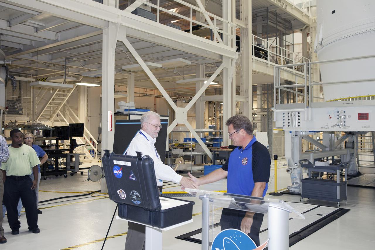 CAPE CANAVERAL, Fla. – Inside the Neil Armstrong Operations and Checkout Building high bay at NASA's Kennedy Space Center in Florida, Jules Schneider, at right, Lockheed Martin Orion Production Operations manager, shakes hands with Blake Hale, Lockheed Martin Ground Operations manager, during a ceremony to officially turn over the Orion spacecraft for Exploration Flight Test-1 to Lockheed Martin Ground Operations. Orion is the exploration spacecraft designed to carry astronauts to destinations not yet explored by humans, including an asteroid and Mars. It will have emergency abort capability, sustain the crew during space travel and provide safe re-entry from deep space return velocities. The first unpiloted test flight of the Orion is scheduled to launch atop a United Launch Alliance Delta IV Heavy rocket from Cape Canaveral Air Force Station in Florida in December to an altitude of 3,600 miles above the Earth's surface. The two-orbit, four-hour flight test will help engineers evaluate the systems critical to crew safety including the heat shield, parachute system and launch abort system. For more information, visit http://www.nasa.gov/orion. Photo credit: NASA/Daniel Casper