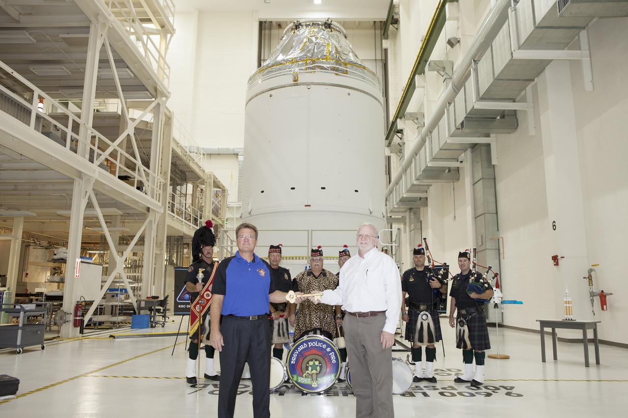 CAPE CANAVERAL, Fla. – During a ceremony inside the Neil Armstrong Operations and Checkout Building high bay at NASA's Kennedy Space Center in Florida, the Orion spacecraft for Exploration Flight Test-1 was officially turned over to Lockheed Martin Ground Operations from Orion Assembly, Integration and Production. Shaking hands during the turn over, are Jules Schneider, at left, Lockheed Martin Orion Production Operations manager, and Blake Hale, Lockheed Martin Ground Operations manager. Behind them are members of the Brevard Police and Fire Pipes and Drums.    Orion is the exploration spacecraft designed to carry astronauts to destinations not yet explored by humans, including an asteroid and Mars. It will have emergency abort capability, sustain the crew during space travel and provide safe re-entry from deep space return velocities. The first unpiloted test flight of the Orion is scheduled to launch atop a United Launch Alliance Delta IV Heavy rocket from Cape Canaveral Air Force Station in Florida in December to an altitude of 3,600 miles above the Earth's surface. The two-orbit, four-hour flight test will help engineers evaluate the systems critical to crew safety including the heat shield, parachute system and launch abort system. For more information, visit http://www.nasa.gov/orion. Photo credit: NASA/Daniel Casper