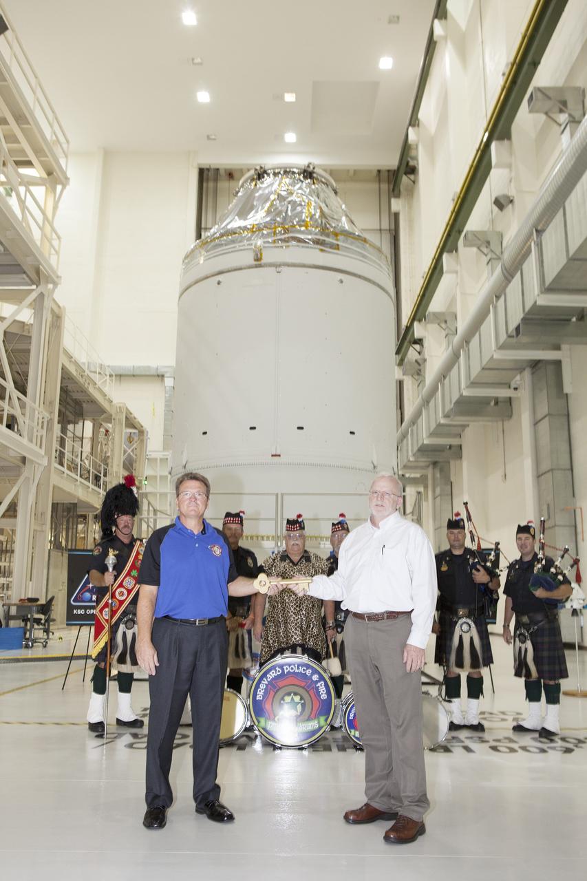 CAPE CANAVERAL, Fla. – During a ceremony inside the Neil Armstrong Operations and Checkout Building high bay at NASA's Kennedy Space Center in Florida, the Orion spacecraft for Exploration Flight Test-1 was officially turned over to Lockheed Martin Ground Operations from Orion Assembly, Integration and Production. Holding the key during the turn over, are Jules Schneider, at left, Lockheed Martin Orion Production Operations manager, and Blake Hale, Lockheed Martin Ground Operations manager. Behind them are members of the Brevard Police and Fire Pipes and Drums.    Orion is the exploration spacecraft designed to carry astronauts to destinations not yet explored by humans, including an asteroid and Mars. It will have emergency abort capability, sustain the crew during space travel and provide safe re-entry from deep space return velocities. The first unpiloted test flight of the Orion is scheduled to launch atop a United Launch Alliance Delta IV Heavy rocket from Cape Canaveral Air Force Station in Florida in December to an altitude of 3,600 miles above the Earth's surface. The two-orbit, four-hour flight test will help engineers evaluate the systems critical to crew safety including the heat shield, parachute system and launch abort system. For more information, visit http://www.nasa.gov/orion. Photo credit: NASA/Daniel Casper