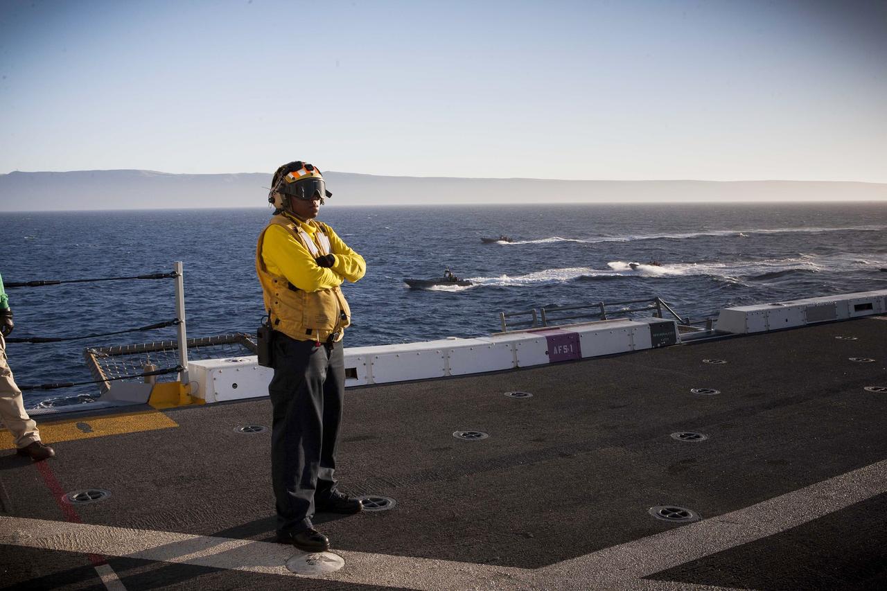 SAN DIEGO, Calif. – A member of the U.S. Navy stands on the deck of the USS Anchorage on the first day of Orion Underway Recovery Test 3 in the Pacific Ocean. In the water are several Zodiac boats and rigid hull inflatable boats with U.S. Navy personnel and divers that are preparing to recover the Orion boilerplate test vehicle already in the water. NASA, Lockheed Martin and U.S. Navy personnel are conducting the recovery test to prepare for recovery of the Orion crew module on its return from a deep space mission. The test will allow the teams to demonstrate and evaluate the recovery processes, procedures, hardware and personnel in open waters. The Ground Systems Development and Operations Program is conducting the underway recovery tests. Orion is the exploration spacecraft designed to carry astronauts to destinations not yet explored by humans, including an asteroid and Mars. It will have emergency abort capability, sustain the crew during space travel and provide safe re-entry from deep space return velocities. The first unpiloted test flight of Orion is scheduled to launch in 2014 atop a United Launch Alliance Delta IV Heavy rocket and in 2018 on NASA’s Space Launch System rocket. For more information, visit http://www.nasa.gov/orion. Photo credit: NASA/Cory Huston