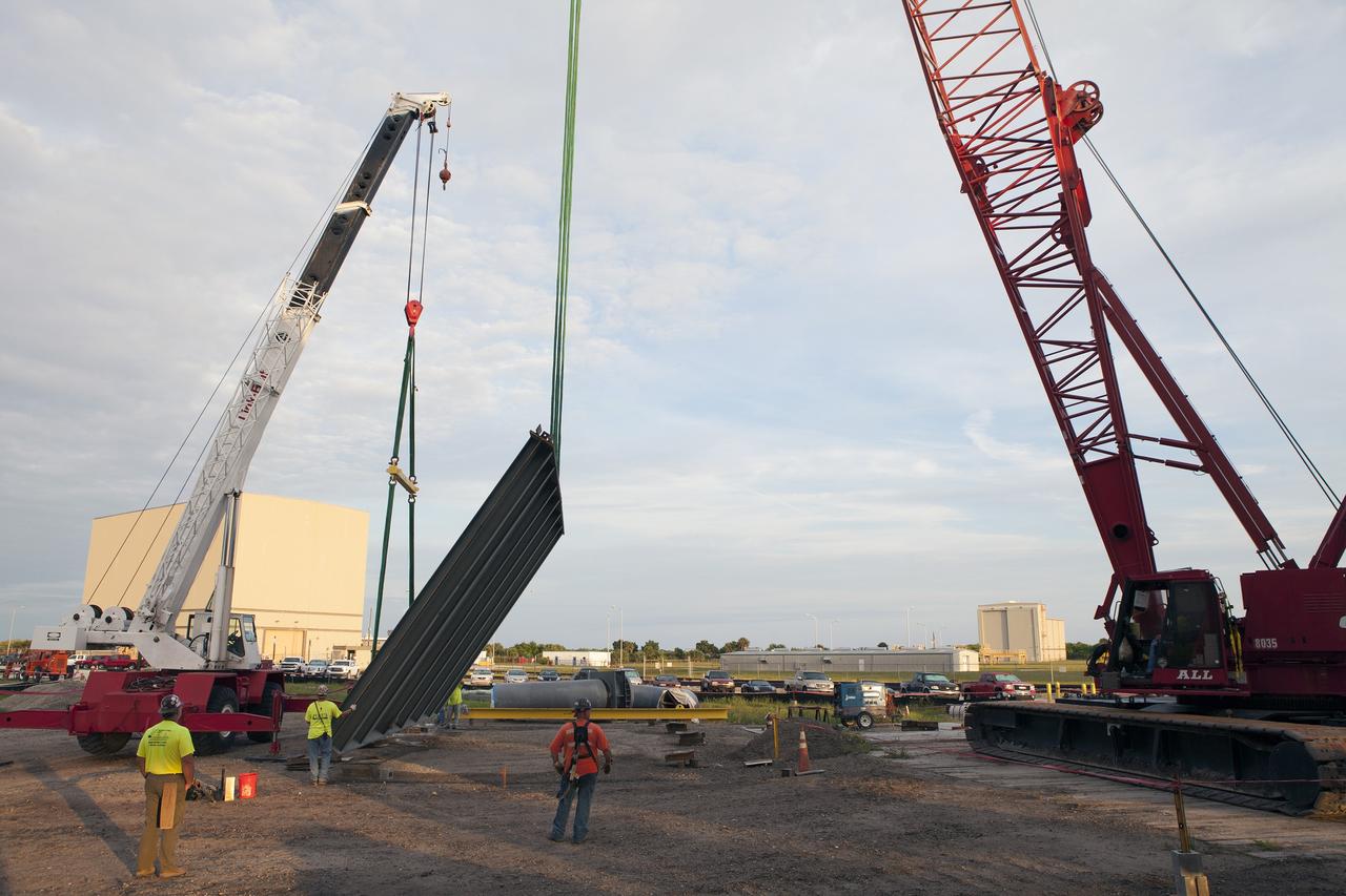 CAPE CANAVERAL, Fla. – Construction workers watch as a crane is used to lift the final large steel beam for installation on the base of the Mobile Launcher, or ML, at the Mobile Launcher Park Site at NASA’s Kennedy Space Center in Florida. The ML is being modified and strengthened to accommodate the weight, size and thrust at launch of NASA's Space Launch System, or SLS, and Orion spacecraft.    In 2013, the agency awarded a contract to J.P. Donovan Construction Inc. of Rockledge, Fla., to modify the ML, which is one of the key elements of ground support equipment that is being upgraded by the Ground Systems Development and Operations Program at Kennedy. The existing 24-foot exhaust hole is being enlarged and strengthened for the larger, heavier SLS rocket. The ML will carry the SLS rocket and Orion spacecraft to Launch Pad 39B for its first uncrewed mission, Exploration Mission-1, in 2018. Photo credit: NASA/Daniel Casper