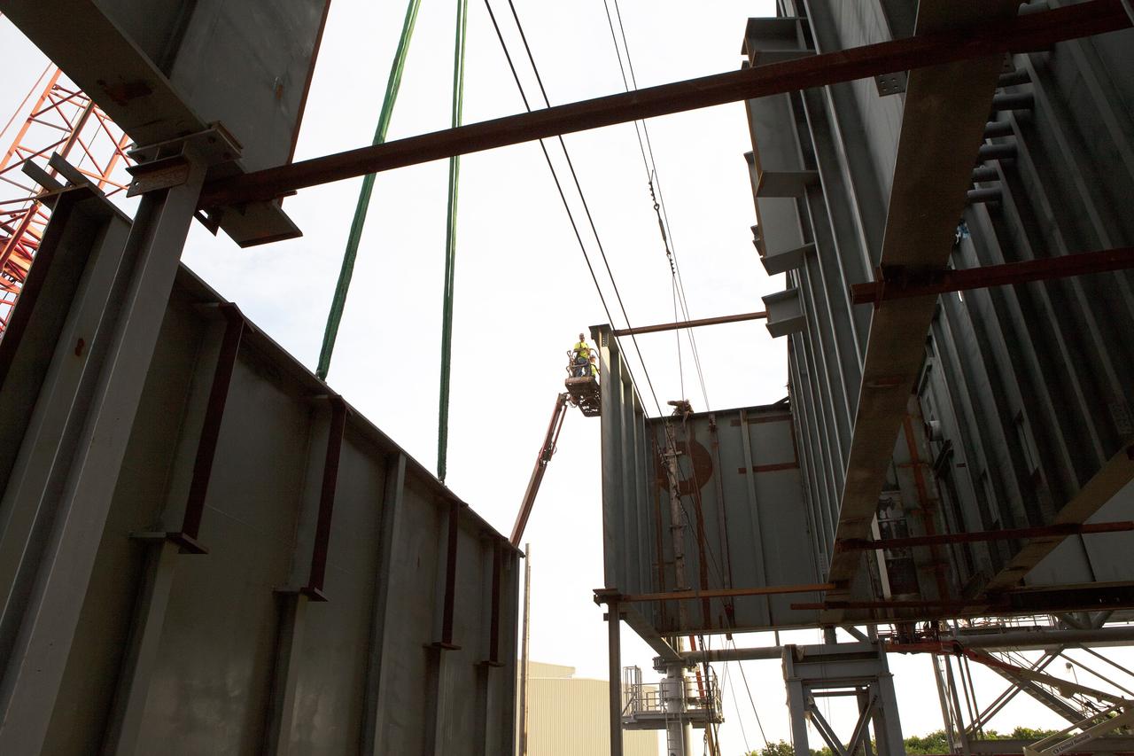 CAPE CANAVERAL, Fla. – Modifications continue on the Mobile Launcher, or ML, at the Mobile Launcher Park Site at NASA’s Kennedy Space Center in Florida. A crane is used to bring the final large steel beam close for installation on the base of the ML. The ML is being modified and strengthened to accommodate the weight, size and thrust at launch of NASA's Space Launch System, or SLS, and Orion spacecraft.    In 2013, the agency awarded a contract to J.P. Donovan Construction Inc. of Rockledge, Fla., to modify the ML, which is one of the key elements of ground support equipment that is being upgraded by the Ground Systems Development and Operations Program at Kennedy. The existing 24-foot exhaust hole is being enlarged and strengthened for the larger, heavier SLS rocket. The ML will carry the SLS rocket and Orion spacecraft to Launch Pad 39B for its first uncrewed mission, Exploration Mission-1, in 2018. Photo credit: NASA/Daniel Casper