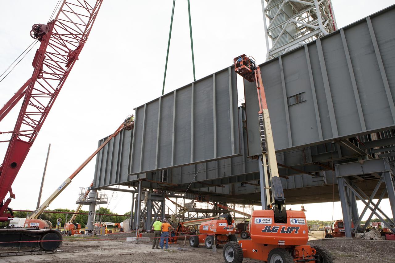 CAPE CANAVERAL, Fla. – Construction workers watch as a crane is used to bring the final large steel beam closer for installation on the base of the Mobile Launcher, or ML, at the Mobile Launcher Park Site at NASA’s Kennedy Space Center in Florida. Workers on lifts are monitoring the progress from above. The ML is being modified and strengthened to accommodate the weight, size and thrust at launch of NASA's Space Launch System, or SLS, and Orion spacecraft.    In 2013, the agency awarded a contract to J.P. Donovan Construction Inc. of Rockledge, Fla., to modify the ML, which is one of the key elements of ground support equipment that is being upgraded by the Ground Systems Development and Operations Program at Kennedy. The existing 24-foot exhaust hole is being enlarged and strengthened for the larger, heavier SLS rocket. The ML will carry the SLS rocket and Orion spacecraft to Launch Pad 39B for its first uncrewed mission, Exploration Mission-1, in 2018. Photo credit: NASA/Daniel Casper