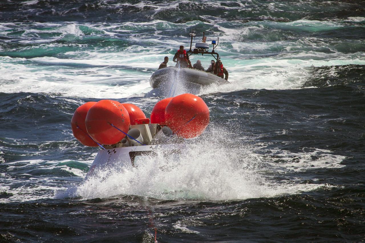 SAN DIEGO, Calif. – A rigid hull inflatable boat containing U.S. Navy divers and other personnel approaches the Orion boilerplate test vehicle floating in the Pacific Ocean, a distance away from the USS Anchorage, during the third day of Orion Underway Recovery Test 3. Orange stabilizers on the top of the test vehicle were inflated to simulate the system that will be used to upright Orion in the water after splashdown.     NASA, Lockheed Martin and U.S. Navy personnel are conducting the recovery test using the test vehicle to prepare for recovery of the Orion crew module on its return from a deep space mission. The test allows the teams to demonstrate and evaluate the recovery processes, procedures, hardware and personnel in open waters. The Ground Systems Development and Operations Program is conducting the underway recovery tests. Orion is the exploration spacecraft designed to carry astronauts to destinations not yet explored by humans, including an asteroid and Mars. It will have emergency abort capability, sustain the crew during space travel and provide safe re-entry from deep space return velocities. The first unpiloted test flight of Orion is scheduled to launch in 2014 atop a United Launch Alliance Delta IV Heavy rocket and in 2018 on NASA’s Space Launch System rocket. For more information, visit http://www.nasa.gov/orion. Photo credit: NASA/Cory Huston