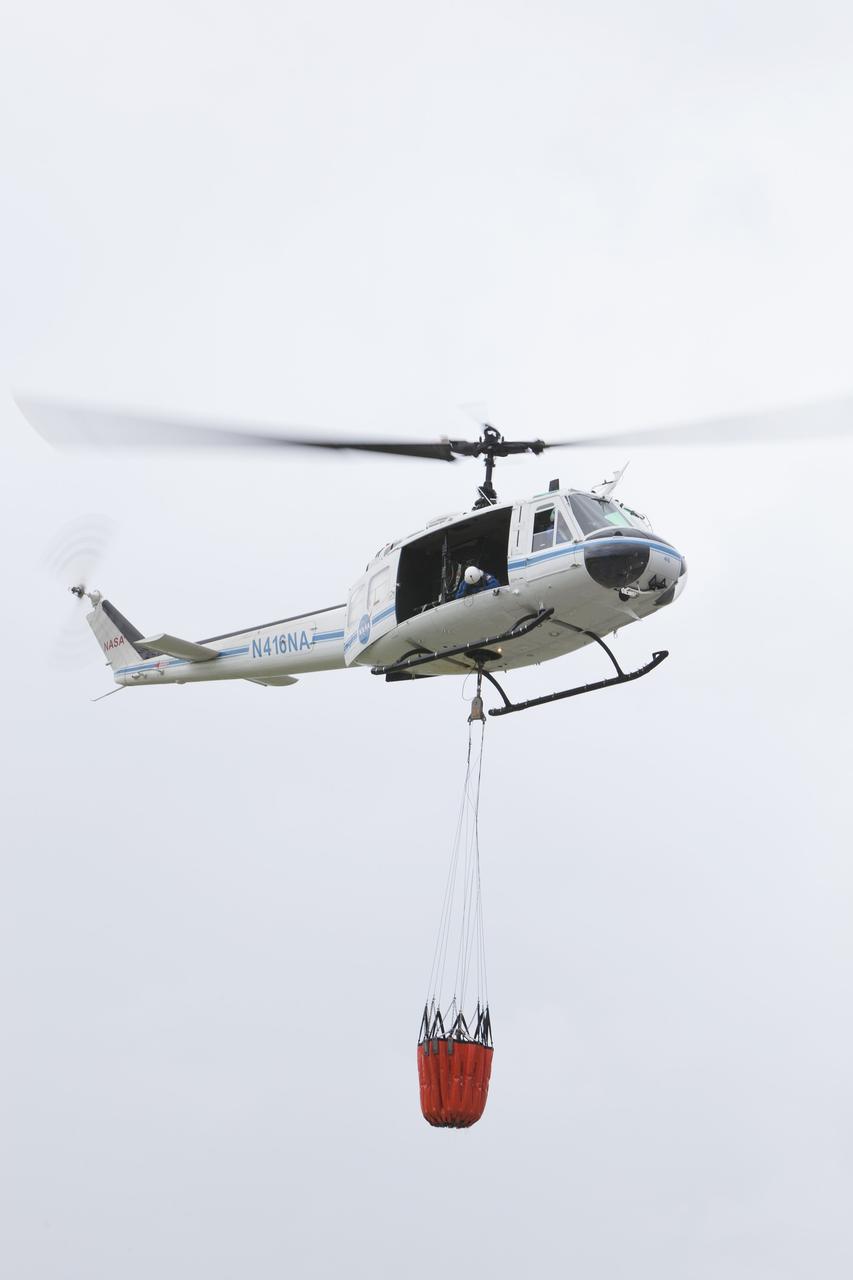 CAPE CANAVERAL, Fla. -- At NASA's Kennedy Space Center in Florida, crew chief Mark Smith of URS looks out the side door down at the Bambi Bucket. Securely strapped to the helicopter floor, his position allows him to tell the pilot precisely when to release the water over the target.      Firefighters respond to wildfires with teams on the ground and in the air. The most up-to-date tools include helicopters that use Bambi Buckets large quantities of water. NASA Flight Operations teams are training to perfect the skills needed to ensure they are ready to use tools, such as the Bambi Bucket, in the event of an out-of-control blaze at the spaceport. Photo credit: NASA/Frankie Martin