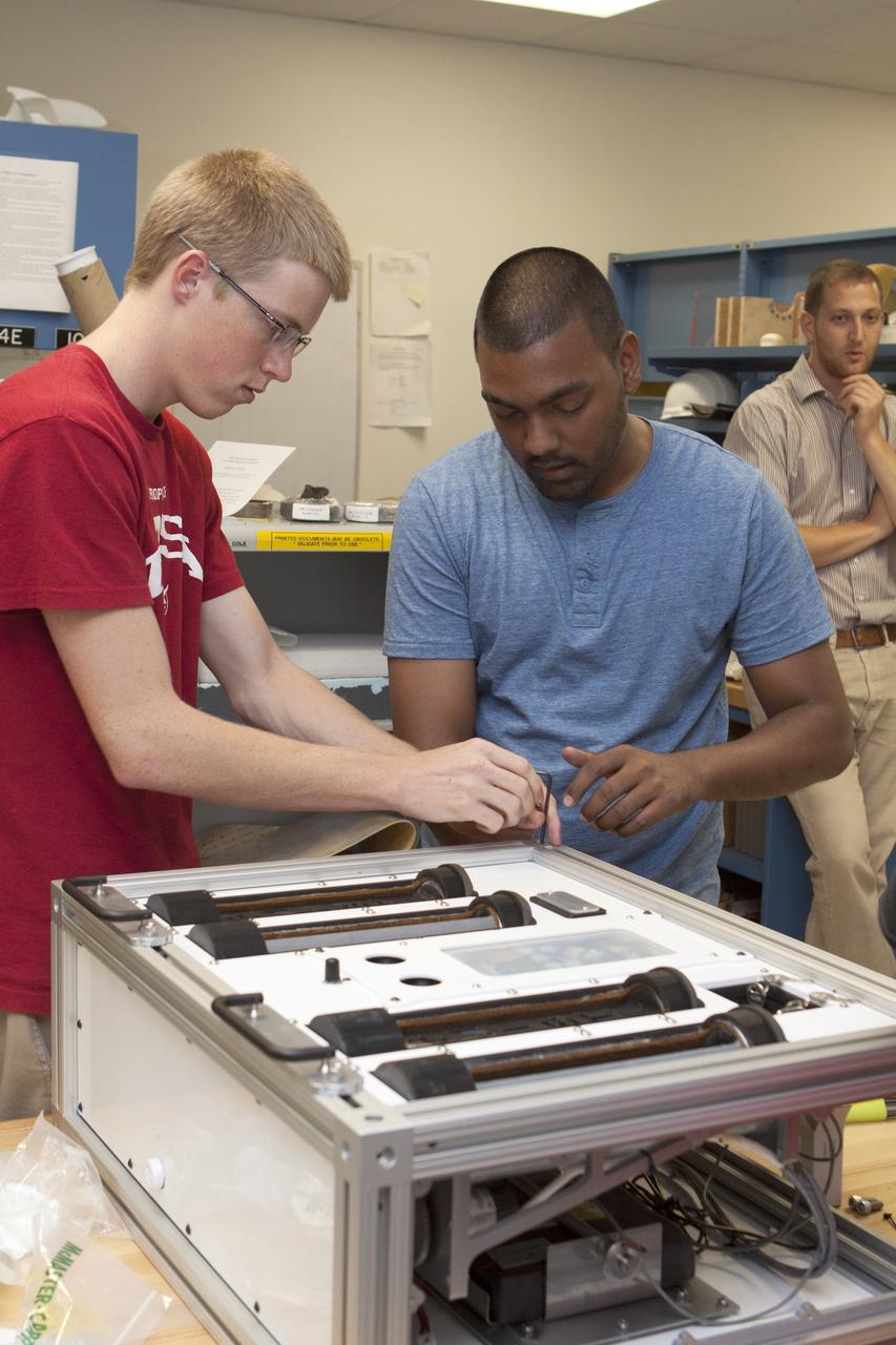 CAPE CANAVERAL, Fla. – Inside the Prototype Laboratory at NASA's Kennedy Space Center in Florida, Evan Williams, left, an Education intern from the University of Central Florida, and Anthony Bharrat, NASA avionics lead, prepare the experiment container for NASA's Exposing Microorganisms in the Stratosphere, or E-MIST, experiment. In the background is David J. Smith, Ph.D., NASA E-MIST principal investigator. The container was designed and built at Kennedy. The 80-pound structure features four doors that rotate to expose up to 10 microbial samples each for a predetermined period of time in the Earth's stratosphere.    The E-MIST experiment will launch on the exterior of a giant scientific balloon gondola at about 8 a.m. MST on Aug. 24 from Ft. Sumner, New Mexico. It will soar 125,000 feet above the Earth during a 5-hour journey over the desert to understand how spore-forming bacteria, commonly found in spacecraft assembly facilities can survive. Photo credit: NASA/Kim Shiflett