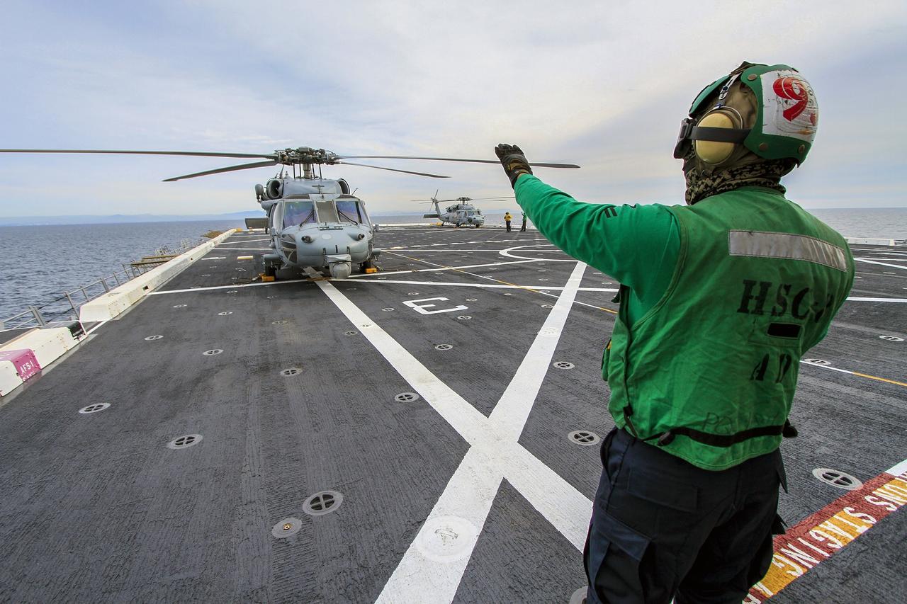 SAN DIEGO, Calif. – A member of the Helicopter Sea Combat Squadron 8 signals to the pilot in an H60-S Seahawk helicopter on the deck of the USS Anchorage as the ship departs Naval Base San Diego in California for the open waters of the Pacific Ocean. NASA and the U.S. Navy are making preparations ahead of Orion's flight test for recovery of the crew module, forward bay cover and parachutes on its return from space and splashdown in the Pacific Ocean. The Ground Systems Development and Operations Program is leading the recovery efforts.    The first unpiloted flight test of Orion is scheduled to launch this week atop a United Launch Alliance Delta IV Heavy rocket. During its two-orbit, 4.5-hour flight, Orion will venture 3,600 miles in altitude and travel nearly 60,000 miles before returning to Earth for a splashdown in the Pacific Ocean. For more information, visit http://www.nasa.gov/orion. Photo credit: NASA/Cory Huston