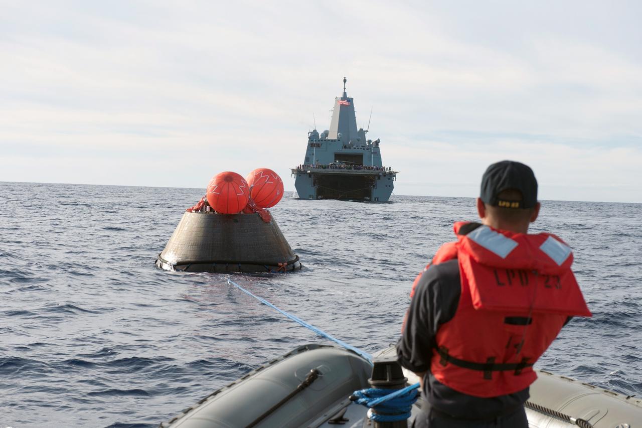 SAN DIEGO, Calif. -- U.S. Navy personnel aboard a rigid hull inflatable boat help recover NASA's Orion spacecraft following its splashdown in the Pacific Ocean after its first flight test in Earth orbit. The USS Anchorage is in the background. NASA, the U.S. Navy and Lockheed Martin are coordinating efforts to recover Orion and secure the spacecraft in the well deck of the USS Anchorage. Orion completed a two-orbit, four-and-a-half hour mission, to test systems critical to crew safety, including the launch abort system, the heat shield and the parachute system. The Ground Systems Development and Operations Program is leading the recovery efforts. For more information, visit www.nasa.gov/orion Photo credit: NASA/Tony Gray