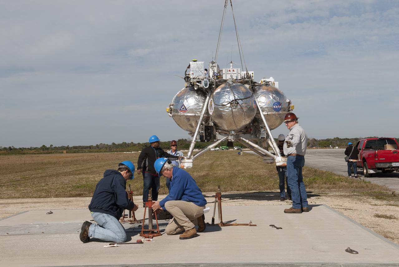 CAPE CANAVERAL, Fla. – Engineers and technicians prepare the launch pad for NASA's Project Morpheus prototype lander at the north end of the Shuttle Landing Facility at NASA's Kennedy Space Center in Florida. Morpheus is being prepared for free flight test number 15 at the SLF. The lander will take off from the ground over a flame trench and use its autonomous landing and hazard avoidance technology, or ALHAT sensors, to survey the hazard field to determine safe landing sites. Project Morpheus tests NASA’s ALHAT and an engine that runs on liquid oxygen and methane, which are green propellants. These new capabilities could be used in future efforts to deliver cargo to planetary surfaces. Project Morpheus is being managed under the Advanced Exploration Systems, or AES, Division in NASA’s Human Exploration and Operations Mission Directorate. For more information on Project Morpheus, visit http://morpheuslander.jsc.nasa.gov/.  Photo credit: NASA/Jim Grossmann