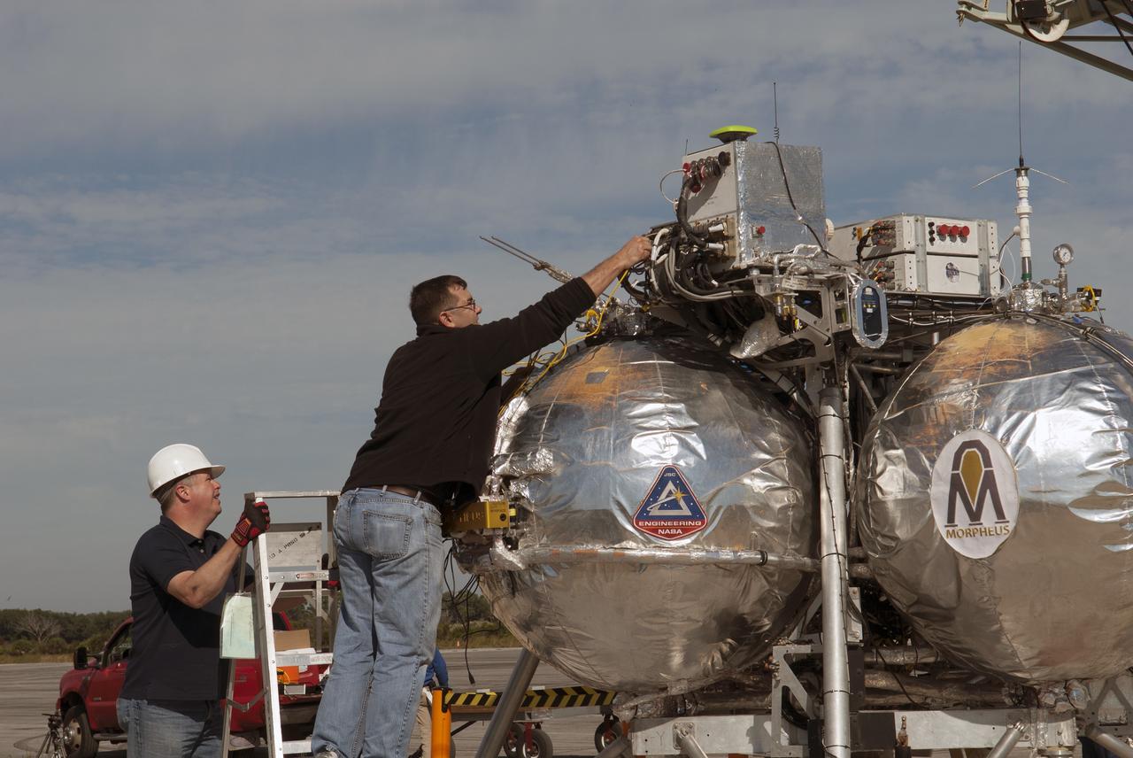 CAPE CANAVERAL, Fla. – Engineers and technicians prepare NASA's Project Morpheus prototype lander for free flight test number 15 at the north end of the Shuttle Landing Facility at NASA's Kennedy Space Center in Florida. The lander will take off from the ground over a flame trench and use its autonomous landing and hazard avoidance technology, or ALHAT sensors, to survey the hazard field to determine safe landing sites. Project Morpheus tests NASA’s ALHAT and an engine that runs on liquid oxygen and methane, which are green propellants. These new capabilities could be used in future efforts to deliver cargo to planetary surfaces. Project Morpheus is being managed under the Advanced Exploration Systems, or AES, Division in NASA’s Human Exploration and Operations Mission Directorate. For more information on Project Morpheus, visit http://morpheuslander.jsc.nasa.gov/.  Photo credit: NASA/Jim Grossmann