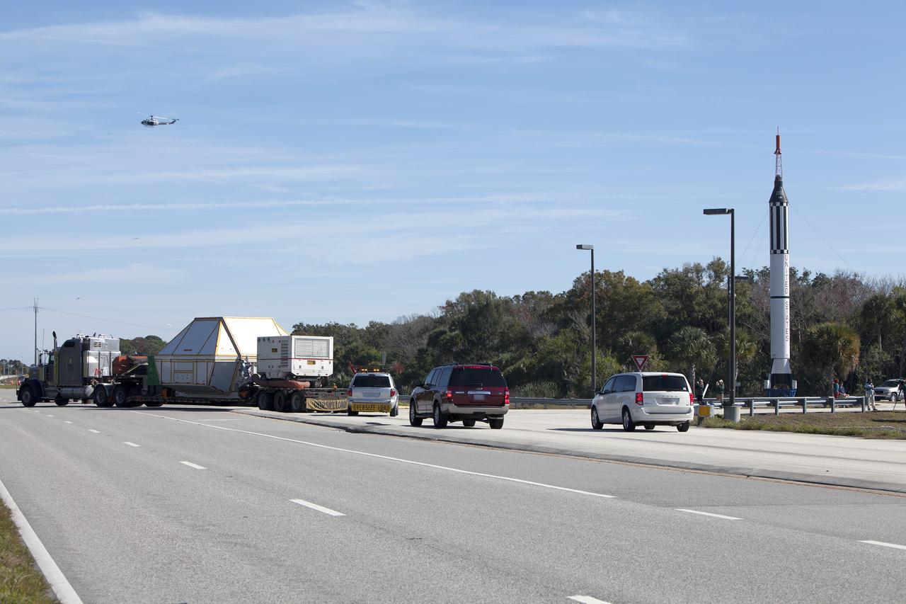 CAPE CANAVERAL, Fla. -- NASA's Orion crew module, enclosed in its crew module transportation fixture and secured on a flatbed truck nears the entrance gate to Kennedy Space Center in Florida. In the background is a full-scale mockup of the Mercury Redstone rocket that boosted NASA astronauts Alan Shepard and Virgil "Gus" Grissom on their 1961 sub-orbital missions that began America's human spaceflight program.  Orion made the overland trip from Naval Base San Diego in California. Orion was recovered from the Pacific Ocean after completing a two-orbit, four-and-a-half hour mission Dec. 5 to test systems critical to crew safety, including the launch abort system, the heat shield and the parachute system. The Ground Systems Development and Operations Program led the recovery, offload and transportation efforts. For more information, visit www.nasa.gov/orion. Photo credit: NASA/Dimitri Gerondidakis
