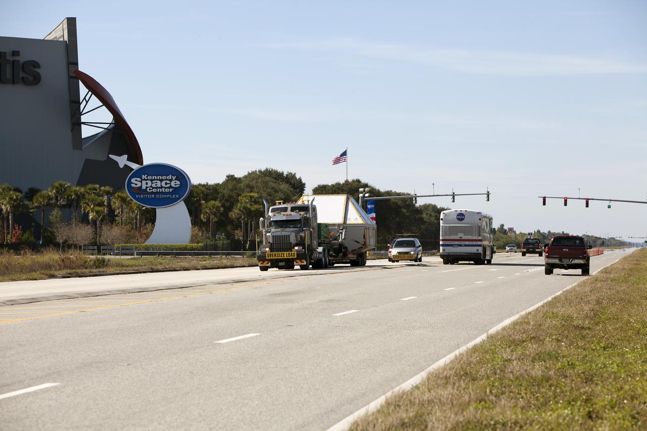 CAPE CANAVERAL, Fla. -- NASA's Orion crew module, enclosed in its crew module transportation fixture and secured on a flatbed truck passes by the Space Shuttle Atlantis building at the Kennedy Space Center Visitor Complex on its way to the entrance gate to Kennedy Space Center in Florida. Orion made the 2,700 mile overland trip from Naval Base San Diego in California. Orion was recovered from the Pacific Ocean after completing a two-orbit, four-and-a-half hour mission Dec. 5 to test systems critical to crew safety, including the launch abort system, the heat shield and the parachute system. The Ground Systems Development and Operations Program led the recovery, offload and transportation efforts. For more information, visit www.nasa.gov/orion. Photo credit: NASA/Dimitri Gerondidakis