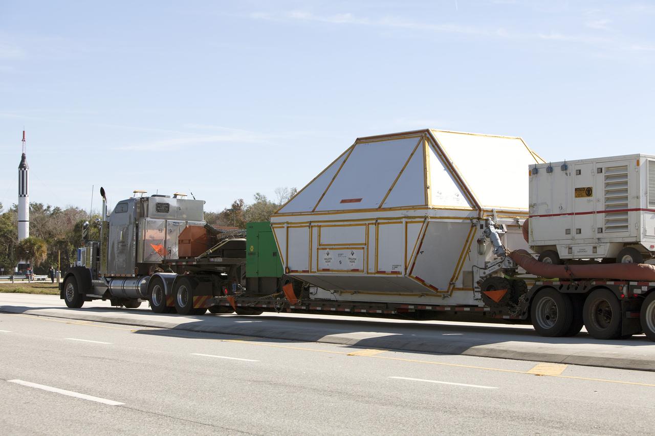 CAPE CANAVERAL, Fla. -- NASA's Orion crew module, enclosed in its crew module transportation fixture and secured on a flatbed truck nears the entrance gate to Kennedy Space Center in Florida. In the background is a full-scale mockup of the Mercury Redstone rocket that boosted NASA astronauts Alan Shepard and Virgil "Gus" Grissom on their 1961 sub-orbital missions that began America's human spaceflight program. Orion made the overland trip from Naval Base San Diego in California. Orion was recovered from the Pacific Ocean after completing a two-orbit, four-and-a-half hour mission Dec. 5 to test systems critical to crew safety, including the launch abort system, the heat shield and the parachute system. The Ground Systems Development and Operations Program led the recovery, offload and transportation efforts. For more information, visit www.nasa.gov/orion. Photo credit: NASA/Dimitri Gerondidakis