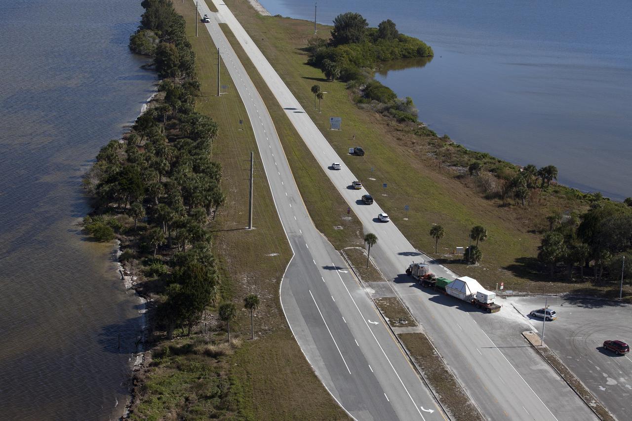 CAPE CANAVERAL, Fla. -- An aerial view near NASA's Kennedy Space Center Visitor Complex reveals the Orion crew module, enclosed in its crew module transportation fixture and secured on a flatbed truck that is proceeding onto the NASA Causeway that leads to the entrance gate to Kennedy Space Center in Florida. Orion made the 2,700 mile overland trip from Naval Base San Diego in California. The spacecraft was recovered from the Pacific Ocean after completing a two-orbit, four-and-a-half hour mission Dec. 5 to test systems critical to crew safety, including the launch abort system, the heat shield and the parachute system. The Ground Systems Development and Operations Program led the recovery, offload and transportation efforts. For more information, visit www.nasa.gov/orion. Photo credit: NASA/Kim Shiflett
