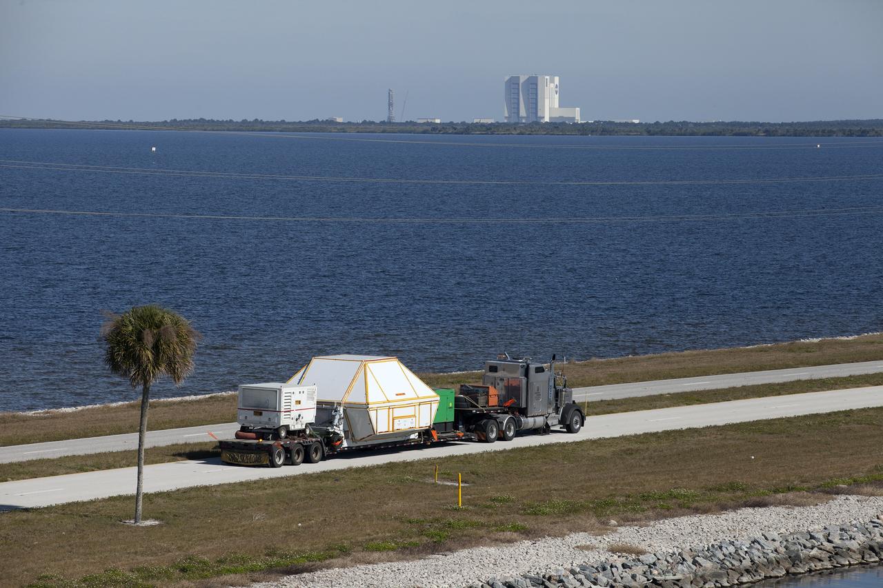 CAPE CANAVERAL, Fla. -- An aerial view near NASA's Kennedy Space Center Visitor Complex reveals the Orion crew module, enclosed in its crew module transportation fixture and secured on a flatbed truck that is proceeding along the NASA Causeway to the entrance gate to Kennedy Space Center in Florida. Across the inland waterway is the iconic Vehicle Assembly Building. Orion made the 2,700 mile overland trip from Naval Base San Diego in California. The spacecraft was recovered from the Pacific Ocean after completing a two-orbit, four-and-a-half hour mission Dec. 5 to test systems critical to crew safety, including the launch abort system, the heat shield and the parachute system. The Ground Systems Development and Operations Program led the recovery, offload and transportation efforts. For more information, visit www.nasa.gov/orion. Photo credit: NASA/Kim Shiflett
