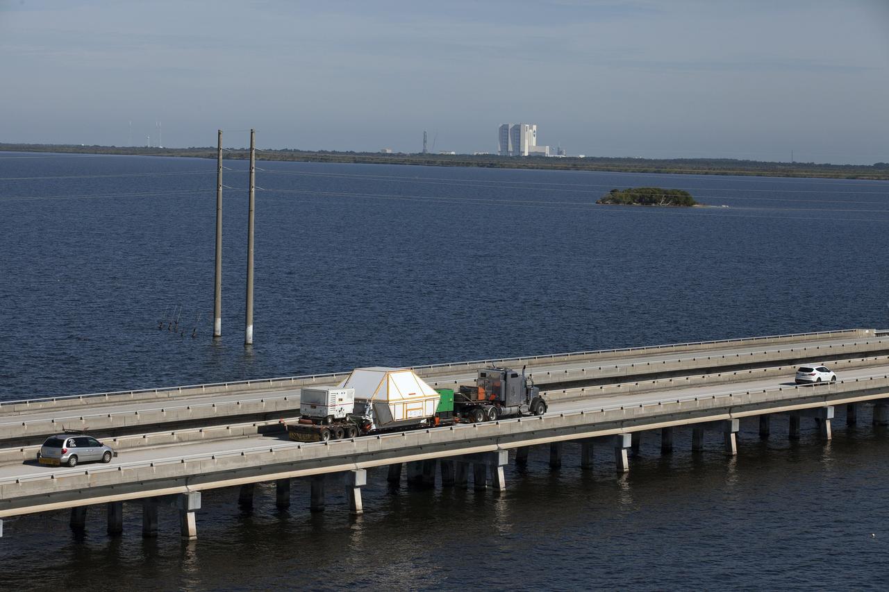 CAPE CANAVERAL, Fla. -- An aerial view near NASA's Kennedy Space Center Visitor Complex reveals the Orion crew module, enclosed in its crew module transportation fixture and secured on a flatbed truck that is proceeding along the NASA Causeway to the entrance gate to Kennedy Space Center in Florida. Across the inland waterway is the iconic Vehicle Assembly Building. Orion made the 2,700 mile overland trip from Naval Base San Diego in California. The spacecraft was recovered from the Pacific Ocean after completing a two-orbit, four-and-a-half hour mission Dec. 5 to test systems critical to crew safety, including the launch abort system, the heat shield and the parachute system. The Ground Systems Development and Operations Program led the recovery, offload and transportation efforts. For more information, visit www.nasa.gov/orion. Photo credit: NASA/Kim Shiflett