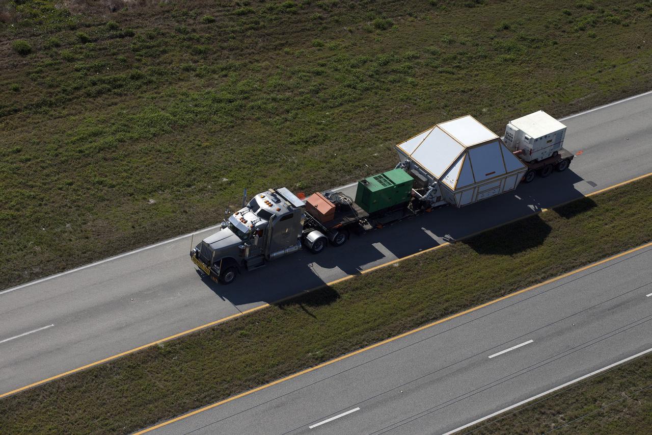 CAPE CANAVERAL, Fla. -- An aerial view near NASA's Kennedy Space Center Visitor Complex reveals the Orion crew module, enclosed in its crew module transportation fixture and secured on a flatbed truck that is proceeding along the NASA Causeway to the entrance gate to Kennedy Space Center in Florida. Orion made the 2,700 mile overland trip from Naval Base San Diego in California. The spacecraft was recovered from the Pacific Ocean after completing a two-orbit, four-and-a-half hour mission Dec. 5 to test systems critical to crew safety, including the launch abort system, the heat shield and the parachute system. The Ground Systems Development and Operations Program led the recovery, offload and transportation efforts. For more information, visit www.nasa.gov/orion. Photo credit: NASA/Kim Shiflett