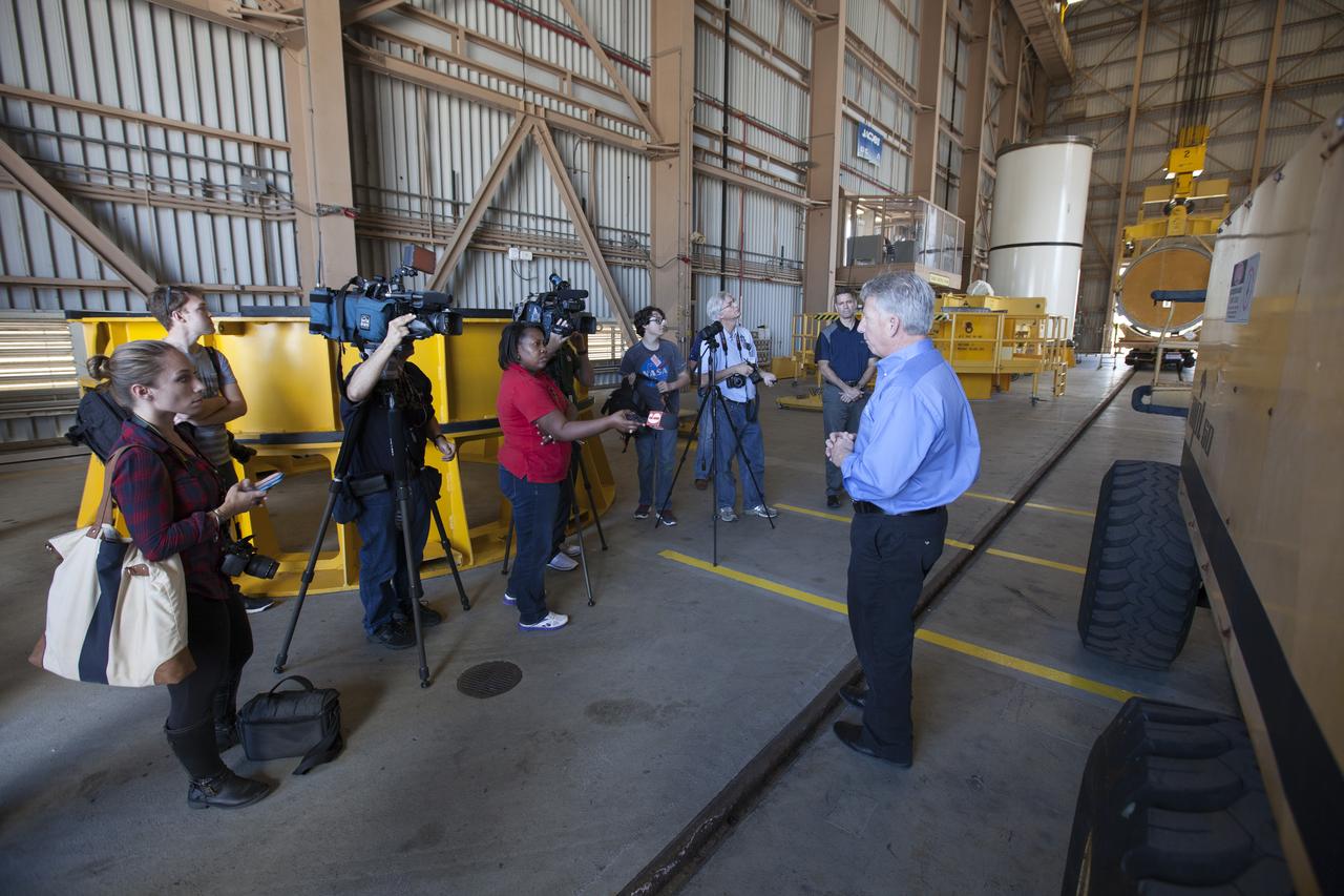 Members of the news media view the high bay inside the Rotation, Processing and Surge Facility (RPSF) at NASA’s Kennedy Space Center in Florida. Kerry Chreist, with Jacobs Engineering on the Test and Operations Support Contract, explains the various test stands and how they will be used to prepare booster segments for NASA’s Space Launch System (SLS) rocket. In the far corner, in the vertical position, is one of two pathfinders, or test versions, of solid rocket booster segments for the SLS rocket. The Ground Systems Development and Operations Program and Jacobs are preparing the booster segments, which are inert, for a series of lifts, moves and stacking operations to prepare for Exploration Mission-1, deep-space missions and the journey to Mars. 