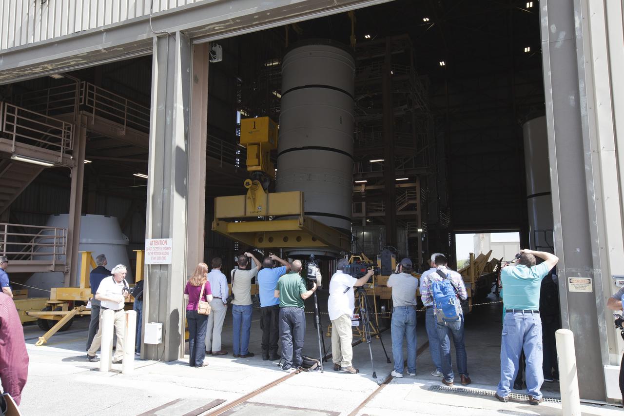 Members of the news media watch as two cranes are used to lift one of two pathfinders, or test versions, of solid rocket booster segments for NASA’s Space Launch System (SLS) rocket into the vertical position inside the Rotation, Processing and Surge Facility at NASA’s Kennedy Space Center in Florida. The pathfinder booster segment will be moved to the other end of the RPSF and secured on a test stand. The Ground Systems Development and Operations Program and Jacobs Engineering, on the Test and Operations Support Contract, will prepare the booster segments, which are inert, for a series of lifts, moves and stacking operations to prepare for Exploration Mission-1, deep-space missions and the journey to Mars. 