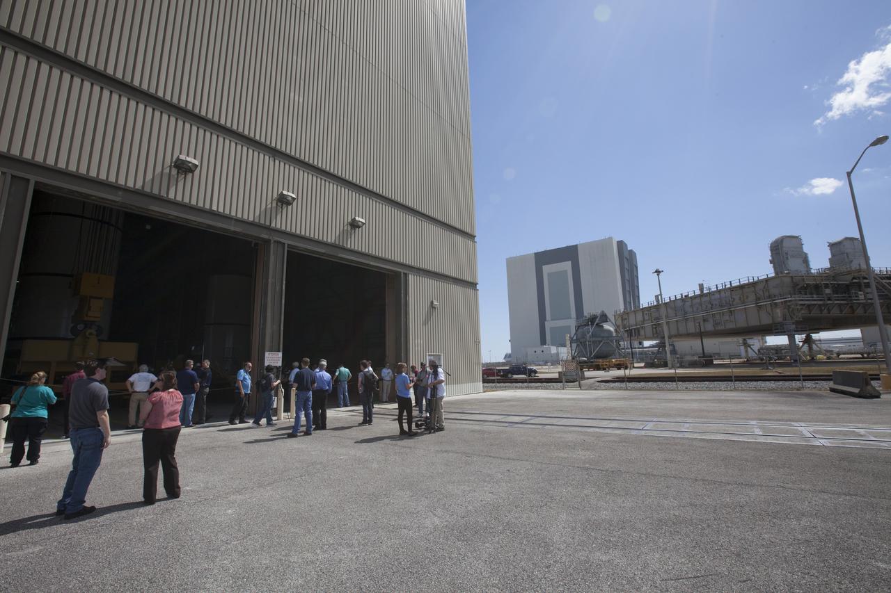 Members of the news media watch as a crane is used to move one of two pathfinders, or test versions, of solid rocket booster segments for NASA’s Space Launch System rocket to a test stand in the Rotation, Processing and Surge Facility at NASA’s Kennedy Space Center in Florida. Inside the RPSF, the Ground Systems Development and Operations Program and Jacobs Engineering, on the Test and Operations Support Contract, will prepare the booster segments, which are inert, for a series of lifts, moves and stacking operations to prepare for Exploration Mission-1, deep-space missions and the journey to Mars. 