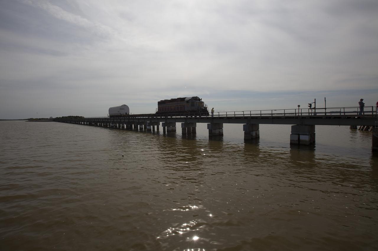 An Iowa Northern locomotive, contracted by Goodloe Transportation of Chicago, travels along the NASA railroad bridge over the Indian River north of Kennedy Space Center, carrying one of two containers on a railcar for transport to the NASA Jay Jay railroad yard. The containers held two pathfinders, or test versions, of solid rocket booster segments for NASA’s Space Launch System rocket that were delivered to the Rotation, Processing and Surge Facility (RPSF). Inside the RPSF, the Ground Systems Development and Operations Program and Jacobs Engineering, on the Test and Operations Support Contract, will conduct a series of lifts, moves and stacking operations using the booster segments, which are inert, to prepare for Exploration Mission-1, deep-space missions and the journey to Mars. The pathfinder booster segments are from Orbital ATK in Utah. 