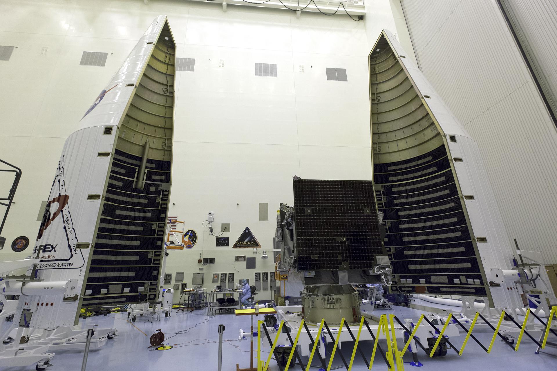 A rocket cone, open into two halves, inside a massive clean room. The OSIRIS-REx spacecraft sits between them, waiting to be encapsulated.