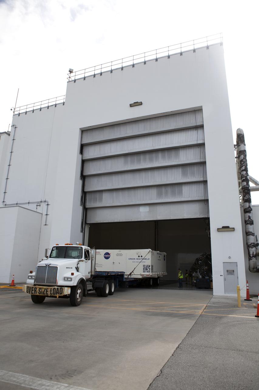 A flatbed truck with the shipping container carrying the Orion heat shield for Exploration Mission 1 (EM-1) arrives at the Neil Armstrong Operations and Checkout Building at NASA’s Kennedy Space Center in Florida. The heat shield arrived aboard the agency’s Super Guppy aircraft at the Shuttle Landing Facility, managed and operated by Space Florida, from Lockheed Martin’s manufacturing facility near Denver. The heat shield will be offloaded and moved into the high bay for processing. The Orion spacecraft will launch atop NASA’s Space Launch System rocket on EM-1, an uncrewed test flight, in 2018. 