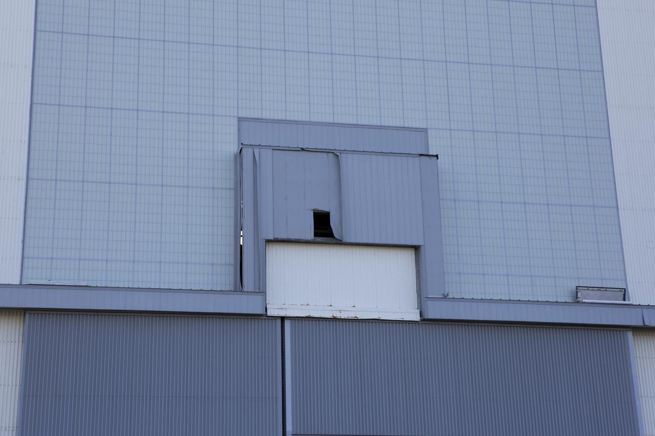 A hole caused by Hurricane Matthew is visible in a section of door on the Vehicle Assembly Building at NASA's Kennedy Space Center in Florida.  Assessments and repairs are in progress at various structures and facilities across the spaceport, part of the ongoing recovery from Hurricane Matthew, which passed to the east of Kennedy on Oct. 6 and 7, 2016. The center received some isolated roof damage, damaged support buildings, a few downed power lines, and limited water intrusion. Beach erosion also occurred, although the storm surge was less than expected.