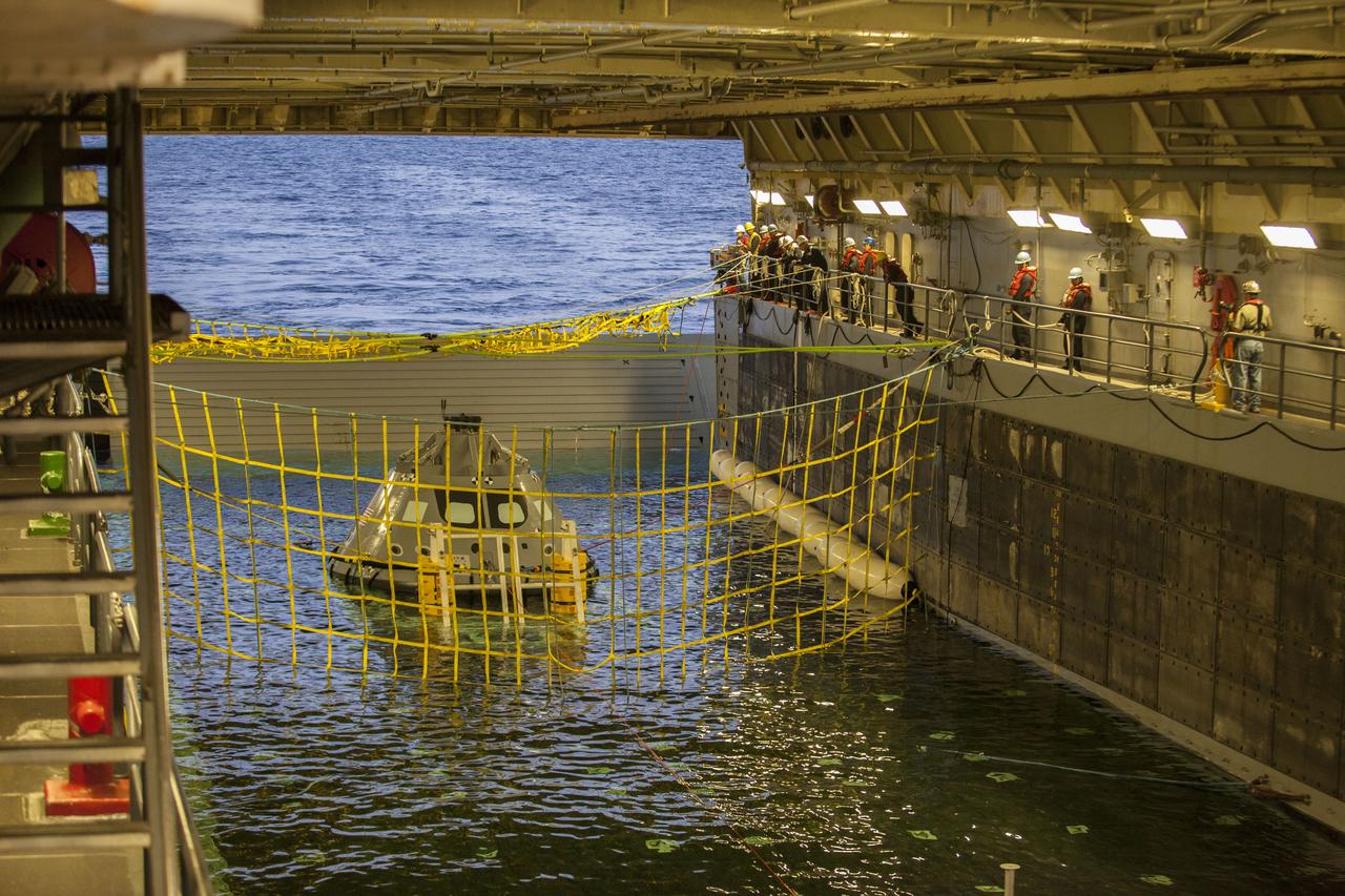 A golden sheen lights up a test version of the Orion crew module in the flooded well deck of the USS San Diego during Underway Recovery Test 5 in the Pacific Ocean off the coast of California. Recovery team personnel have secured a net around the crew module. NASA's Ground Systems Development and Operations Program and the U.S. Navy will conduct a series of tests to prepare for recovery of Orion on its return from deep space missions. The testing will allow the team to demonstrate and evaluate recovery processes, procedures, hardware and personnel in open waters. Orion is the exploration spacecraft designed to carry astronauts to destinations not yet explored by humans, including an asteroid and NASA's Journey to Mars. It will have emergency abort capability, sustain the crew during space travel and provide safe re-entry from deep space return velocities. Orion is scheduled to launch on NASA's Space Launch System in late 2018. For more information, visit http://www.nasa.gov/orion. 