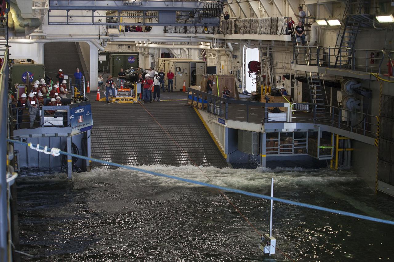In the flooded well deck of the USS San Diego, recovery team members watch as a winch line is operated to help guide a test version of the Orion crew module into the well deck during Orion Underway Recovery Test 5 in the Pacific Ocean off the coast of California. NASA's Ground Systems Development and Operations Program and the U.S. Navy will practice recovery techniques using the well deck of the ship and a test version of the Orion crew module to prepare for recovery of Orion on its return from deep space missions. The testing will allow the team to demonstrate and evaluate recovery processes, procedures, hardware and personnel in open waters. Orion is the exploration spacecraft designed to carry astronauts to destinations not yet explored by humans, including an asteroid and NASA's Journey to Mars. It will have emergency abort capability, sustain the crew during space travel and provide safe re-entry from deep space return velocities. Orion is scheduled to launch on NASA's Space Launch System in late 2018. For more information, visit http://www.nasa.gov/orion.