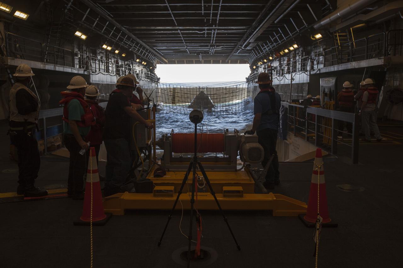 Winch team operators help guide a test version of the Orion crew module in the flooded well deck of the USS San Diego during Underway Recovery Test 5 in the Pacific Ocean off the coast of California. NASA's Ground Systems Development and Operations Program and the U.S. Navy are conducting a series of tests using the ship's well deck, the test module, various watercraft and equipment to prepare for recovery of Orion on its return from deep space missions. The testing will allow the team to demonstrate and evaluate recovery processes, procedures, hardware and personnel in open waters. Orion is the exploration spacecraft designed to carry astronauts to destinations not yet explored by humans, including an asteroid and NASA's Journey to Mars. It will have emergency abort capability, sustain the crew during space travel and provide safe re-entry from deep space return velocities. Orion is scheduled to launch on NASA's Space Launch System in late 2018. For more information, visit http://www.nasa.gov/orion. 