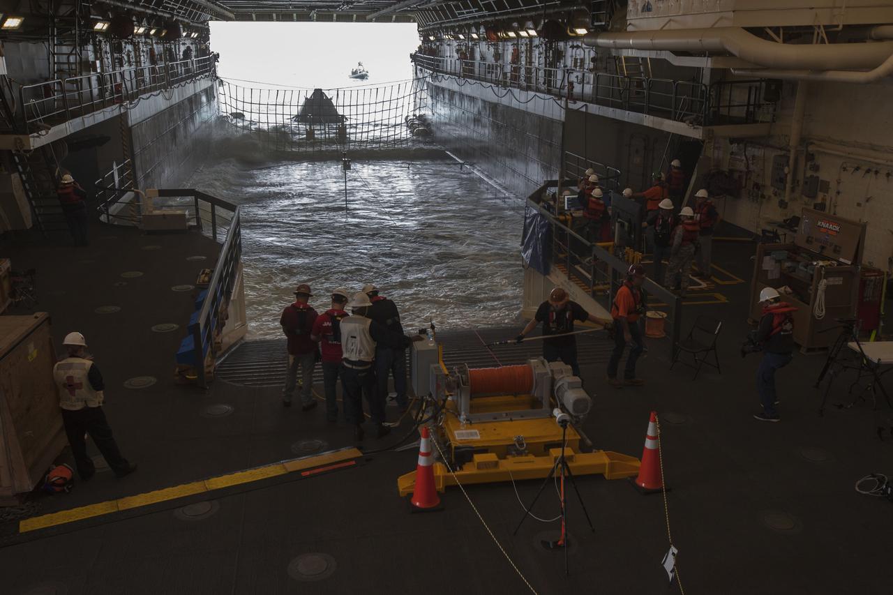 Winch team operators help guide a test version of the Orion crew module into the flooded well deck of the USS San Diego during Underway Recovery Test 5 in the Pacific Ocean off the coast of California. NASA's Ground Systems Development and Operations Program and the U.S. Navy are conducting a series of tests using the ship's well deck, the test module, various watercraft and equipment to prepare for recovery of Orion on its return from deep space missions. The testing will allow the team to demonstrate and evaluate recovery processes, procedures, hardware and personnel in open waters. Orion is the exploration spacecraft designed to carry astronauts to destinations not yet explored by humans, including an asteroid and NASA's Journey to Mars. It will have emergency abort capability, sustain the crew during space travel and provide safe re-entry from deep space return velocities. Orion is scheduled to launch on NASA's Space Launch System in late 2018. For more information, visit http://www.nasa.gov/orion. 