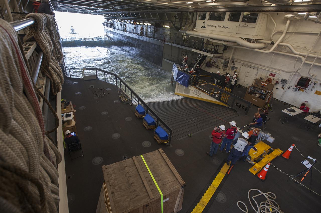 Winch operators, at right, watch from the flooded well deck of the USS San Diego as a test version of the Orion crew module is guided to the well deck during Underway Recovery Test 5 in the Pacific Ocean off the coast of California. NASA's Ground Systems Development and Operations Program and the U.S. Navy are conducting a series of tests using the well deck of the USS San Diego, several watercraft, support equipment and personnel to prepare for recovery of Orion on its return from deep space missions. The testing will allow the team to demonstrate and evaluate recovery processes, procedures, hardware and personnel in open waters. Orion is the exploration spacecraft designed to carry astronauts to destinations not yet explored by humans, including an asteroid and NASA's Journey to Mars. It will have emergency abort capability, sustain the crew during space travel and provide safe re-entry from deep space return velocities. Orion is scheduled to launch on NASA's Space Launch System in late 2018. For more information, visit http://www.nasa.gov/orion. 