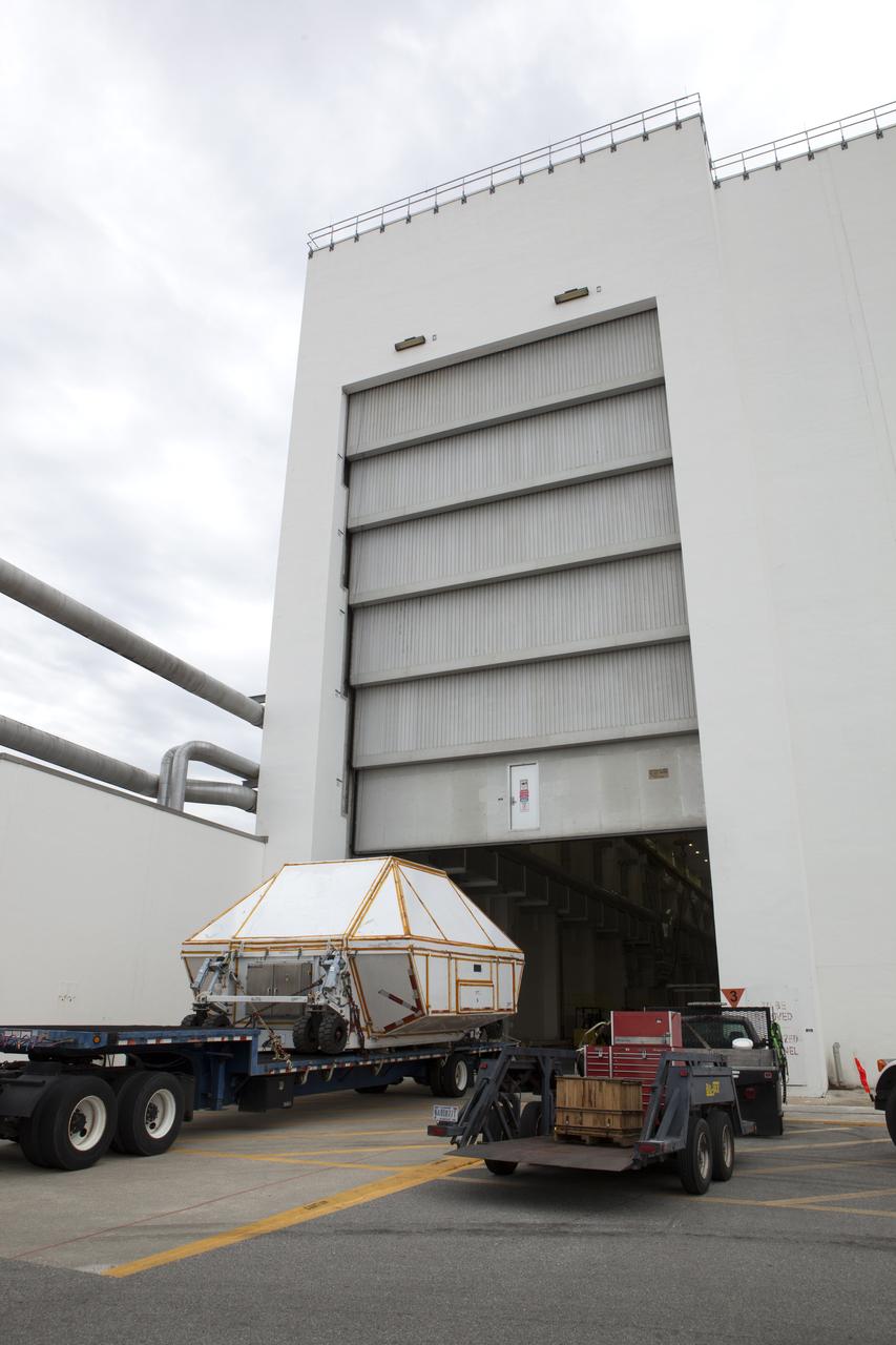 A transporter carrying the Orion crew module structural test article (STA) in its container arrives at the low bay entrance of the Neil Armstrong Operations and Checkout Building at NASA's Kennedy Space Center in Florida. The STA arrived aboard NASA's Super Guppy aircraft at the Shuttle Landing Facility operated by Space Florida. The test article will be moved inside the facility's high bay for further testing. The Orion spacecraft will launch atop NASA’s Space Launch System rocket on EM-1, its first deep space mission, in late 2018.