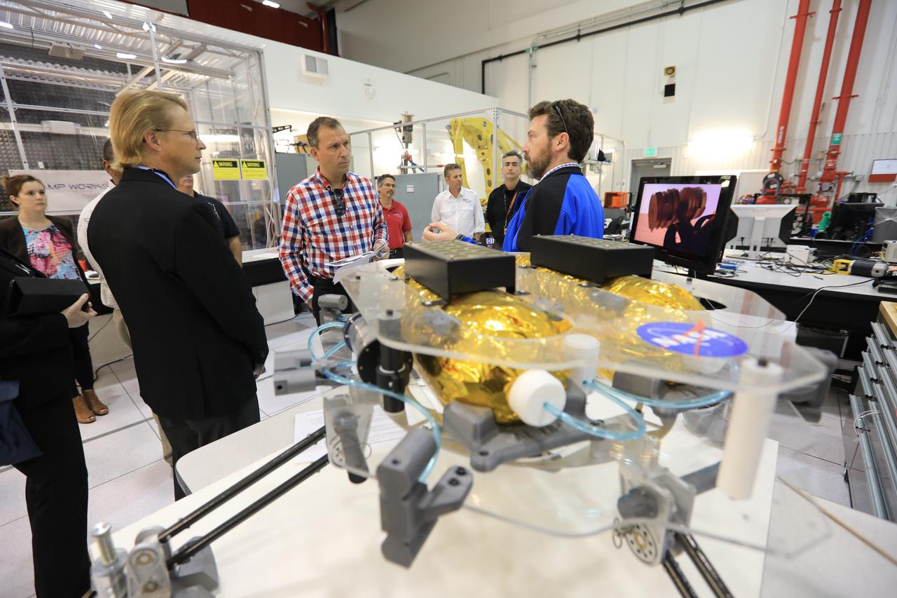 Thomas Zurbuchen, in plaid shirt, NASA's associate administrator for the Science Mission Directorate, listens to a presentation at the Swamp Works facility at NASA's Kennedy Space Center in Florida. In the foreground is a prototype robotic exploration vehicle.